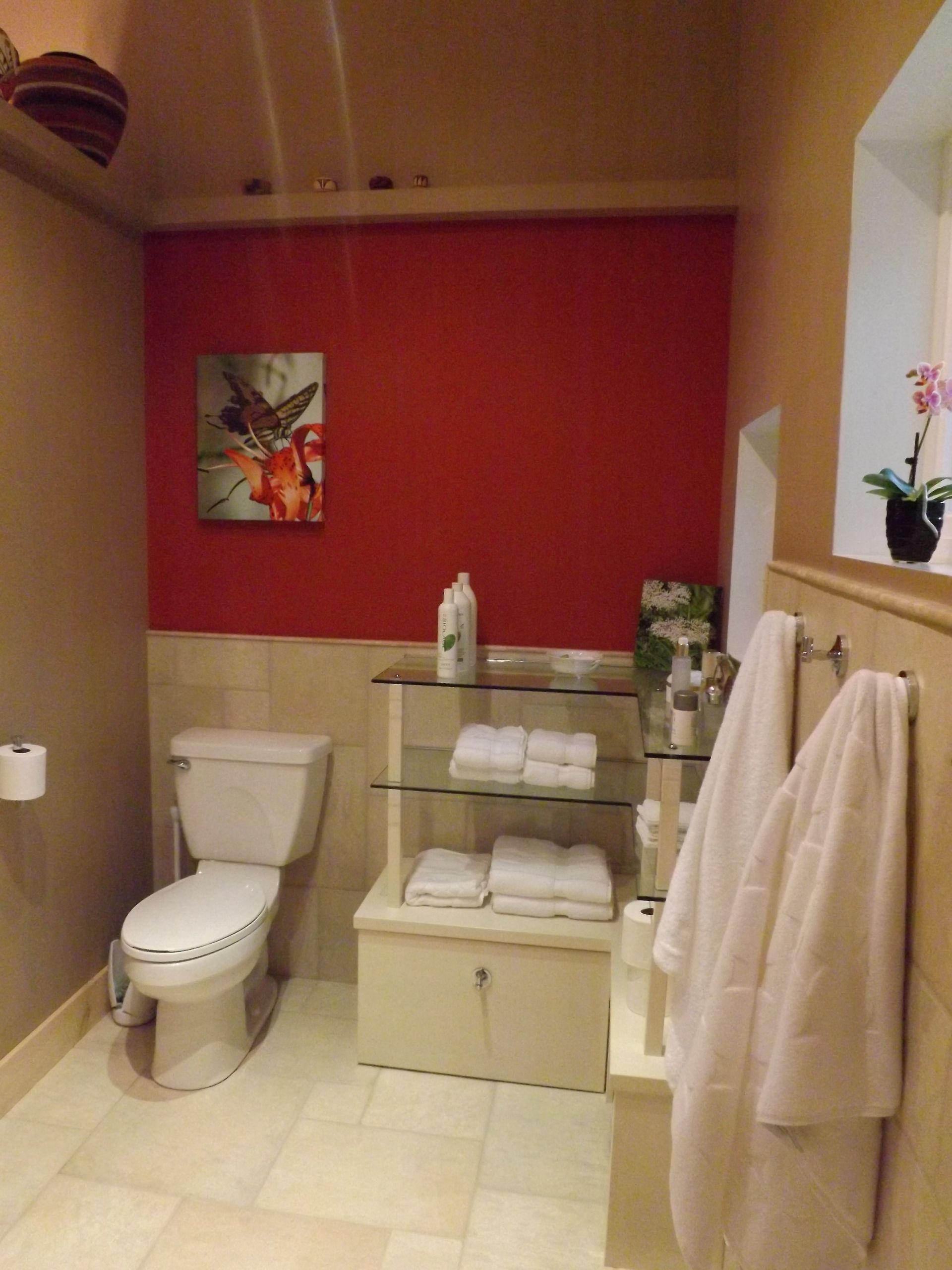 Small bathroom with a toilet, vanity, towels, and red accent wall.