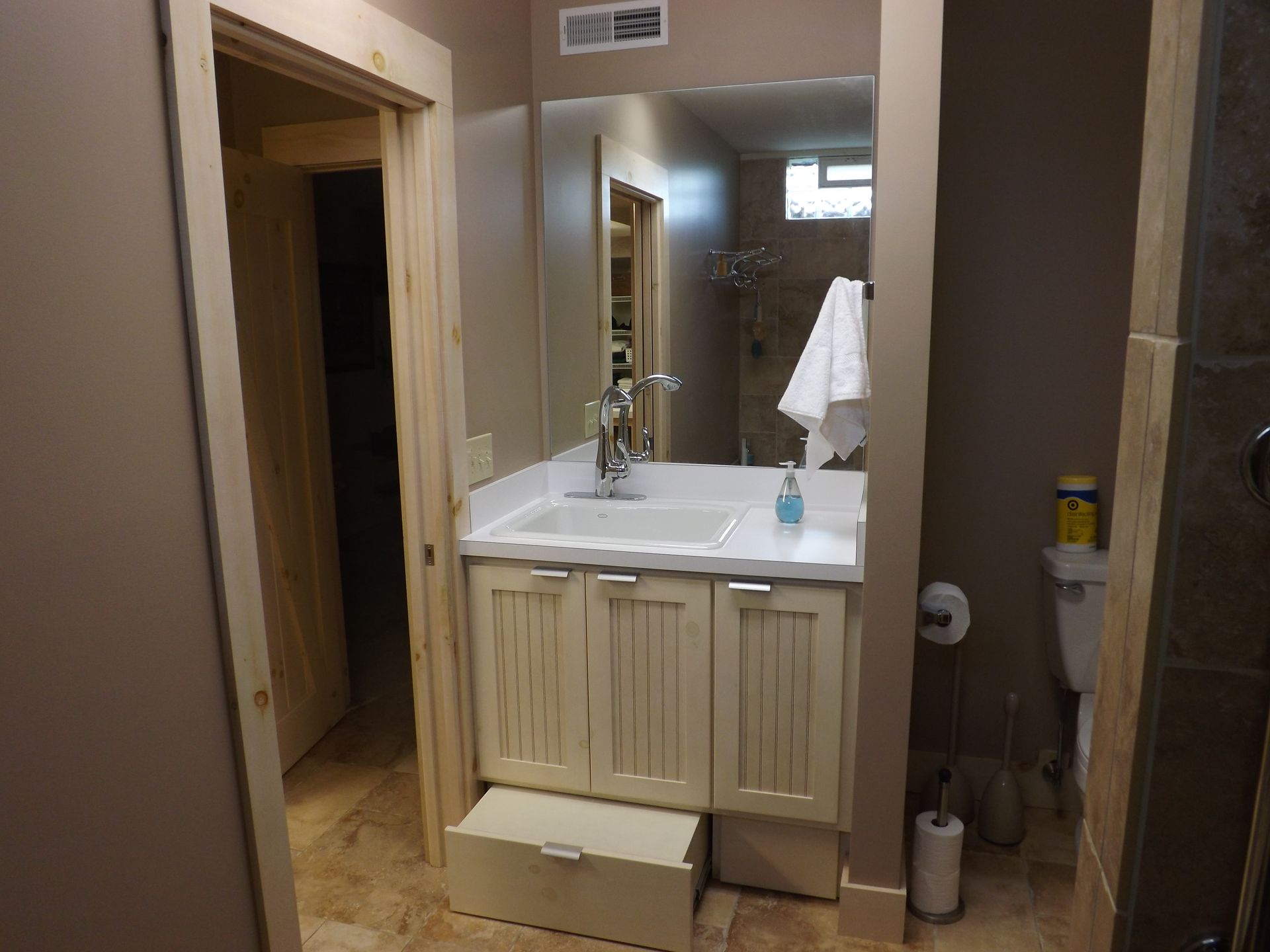 Bathroom vanity with sink and mirror, beige walls, towel hanging nearby, and an open doorway to the left