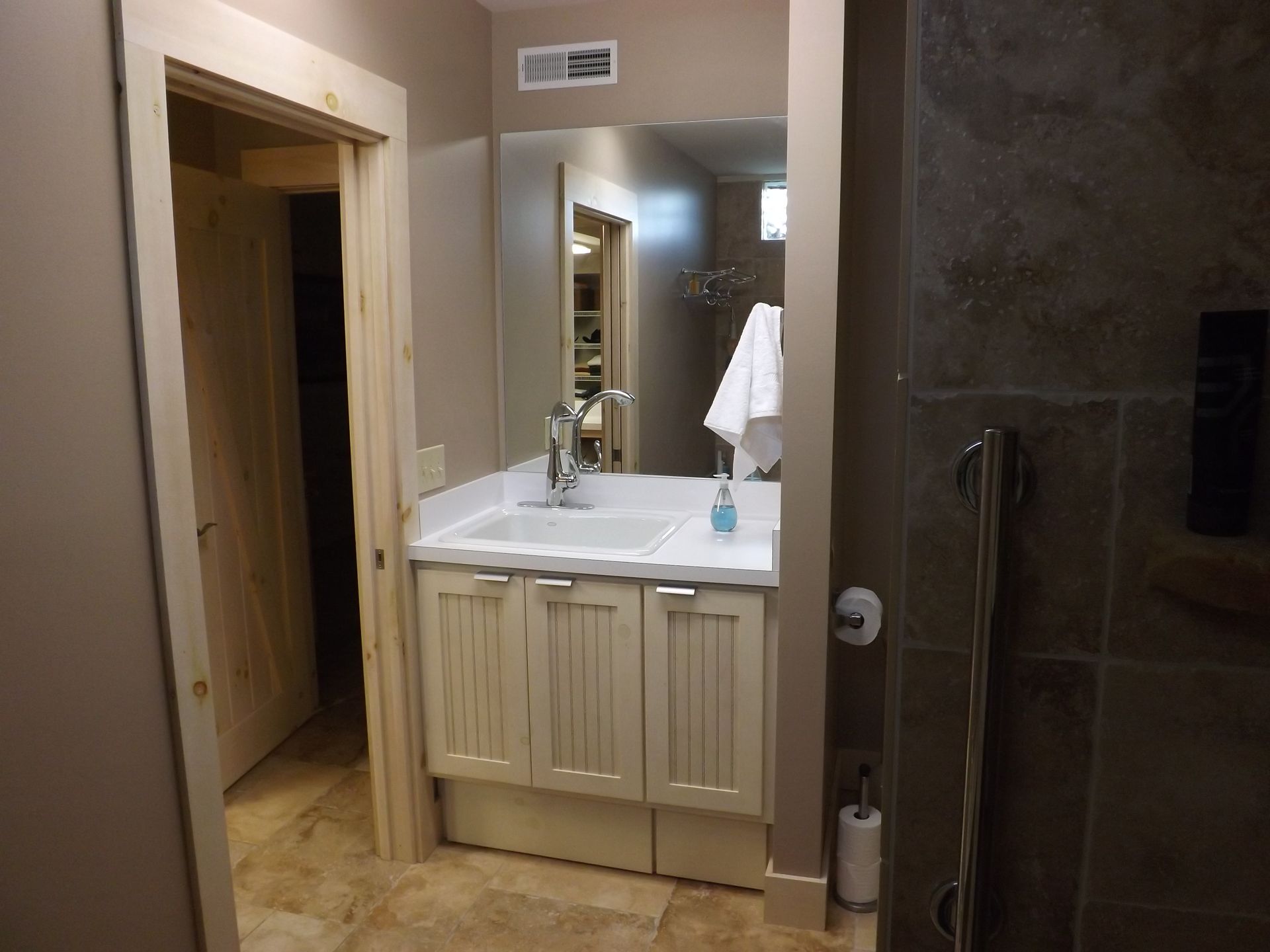 Small bathroom with beige vanity, mirror, sink, towel rack, and open doorway to a hallway.