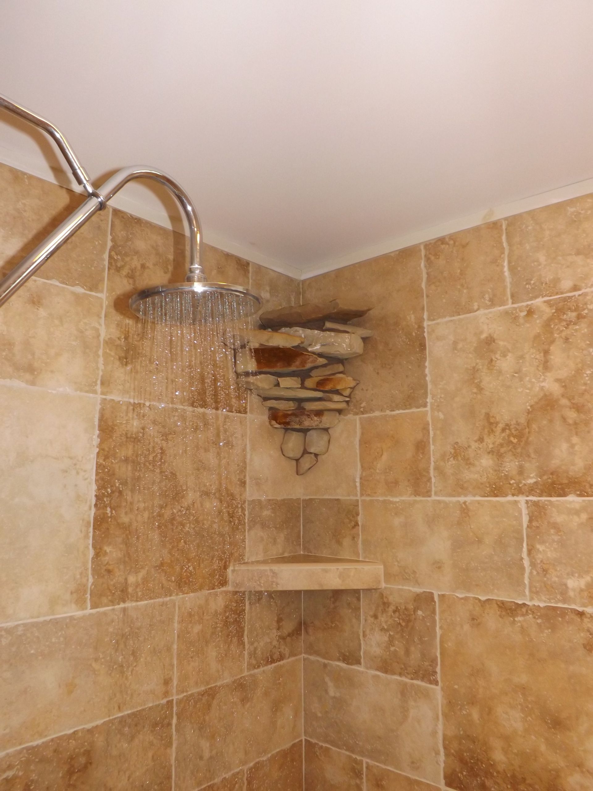 Stone-tiled shower with a chrome showerhead and built-in corner shelf under running water