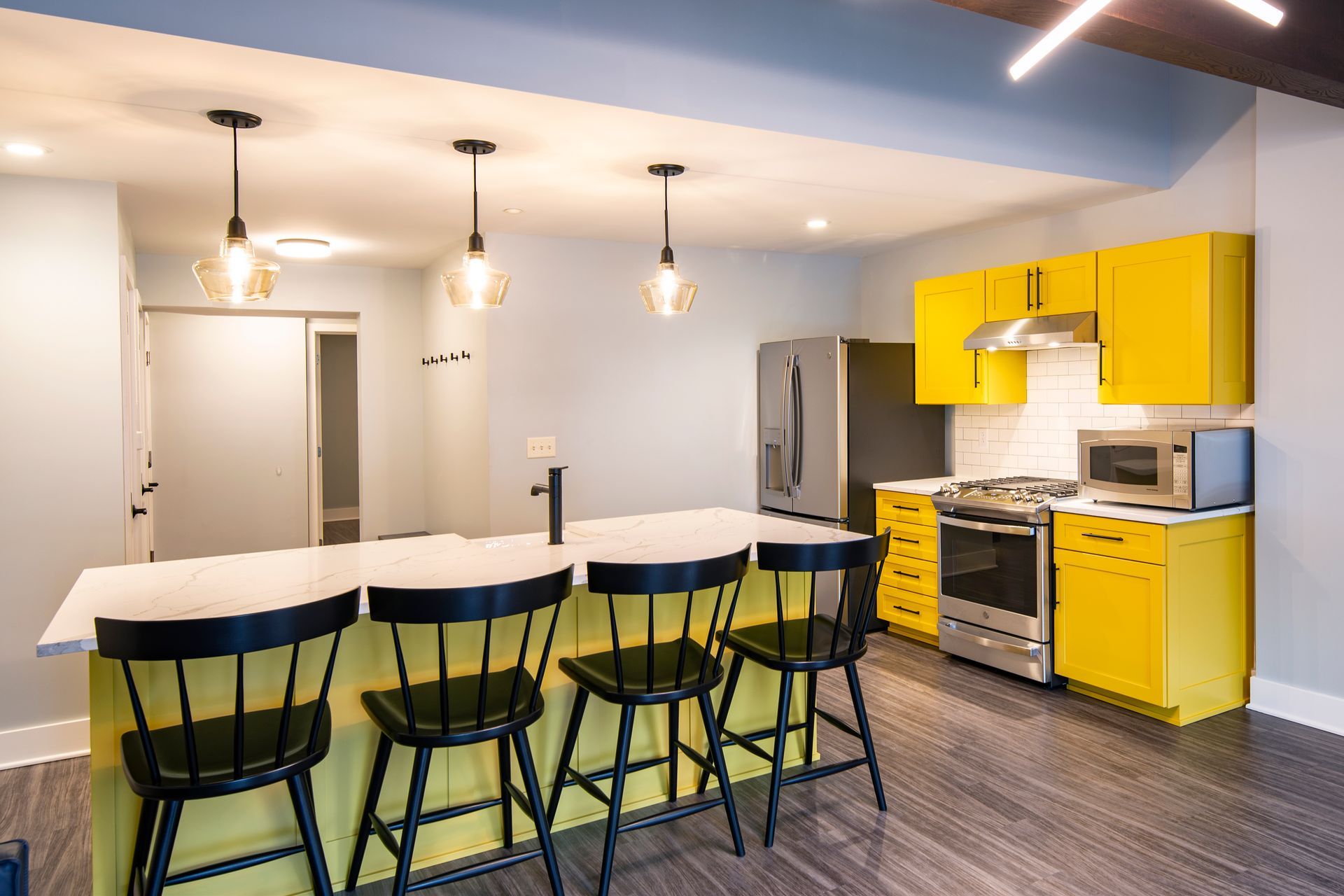 Modern kitchen with yellow cabinets, white island, black stools, and pendant lights