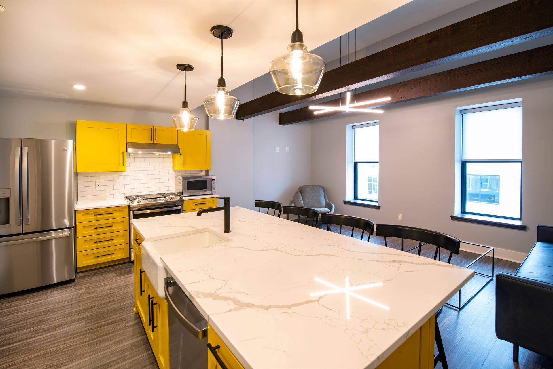 Bright modern kitchen with yellow cabinets, marble island, bar stools, and hanging pendant lights.