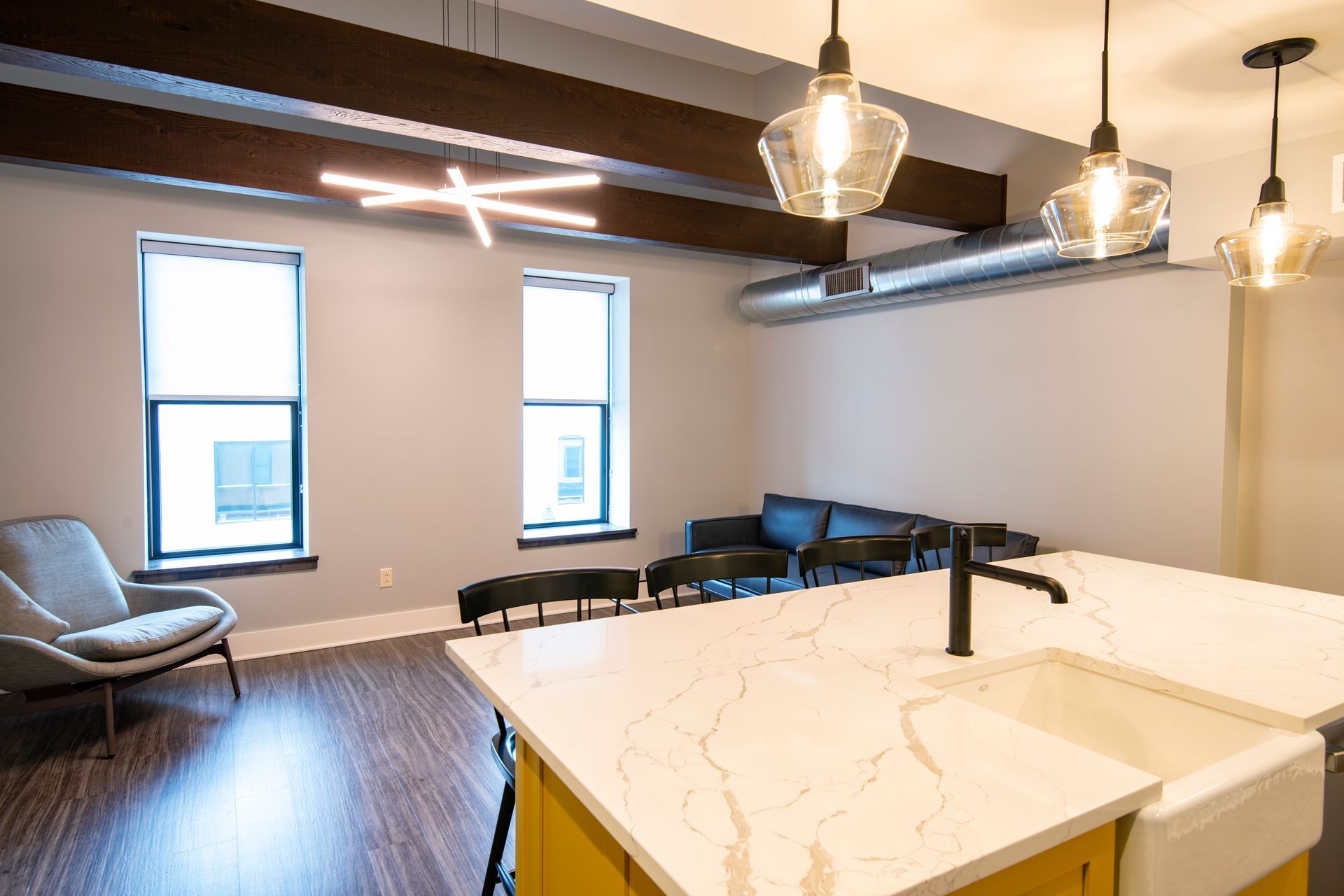 Modern open-plan lounge with sofa, stools, pendant lights, and white kitchen island.