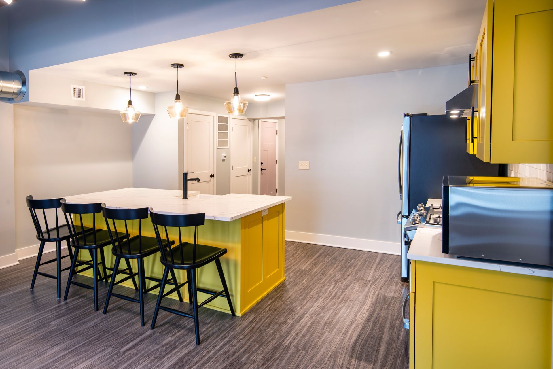 Modern kitchen with yellow cabinets, white island, bar stools, and microwave.