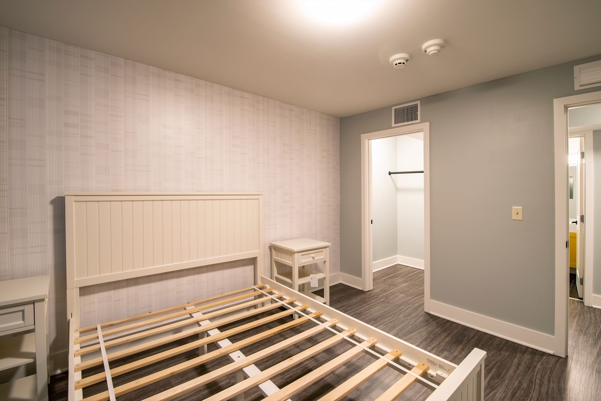 Bed frame in a sparse gray bedroom with wood floors, nightstand, and two open doorways.