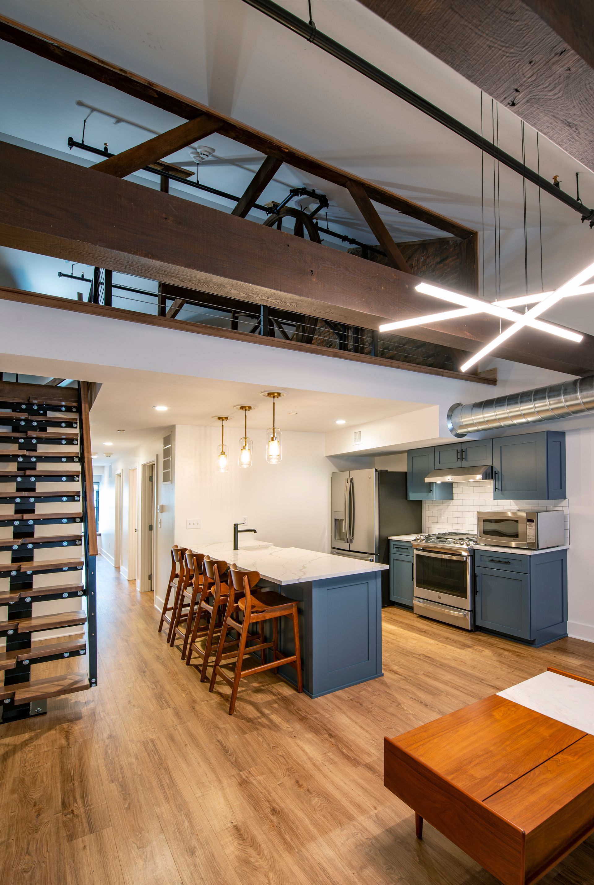 Open-concept loft kitchen and living area with exposed beams, blue cabinets, and dining stools.