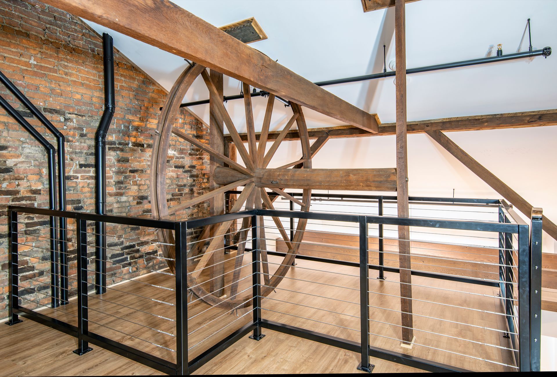 Custom home loft with exposed brick walls, wooden beams, and black metal railings overlooking a lower level.