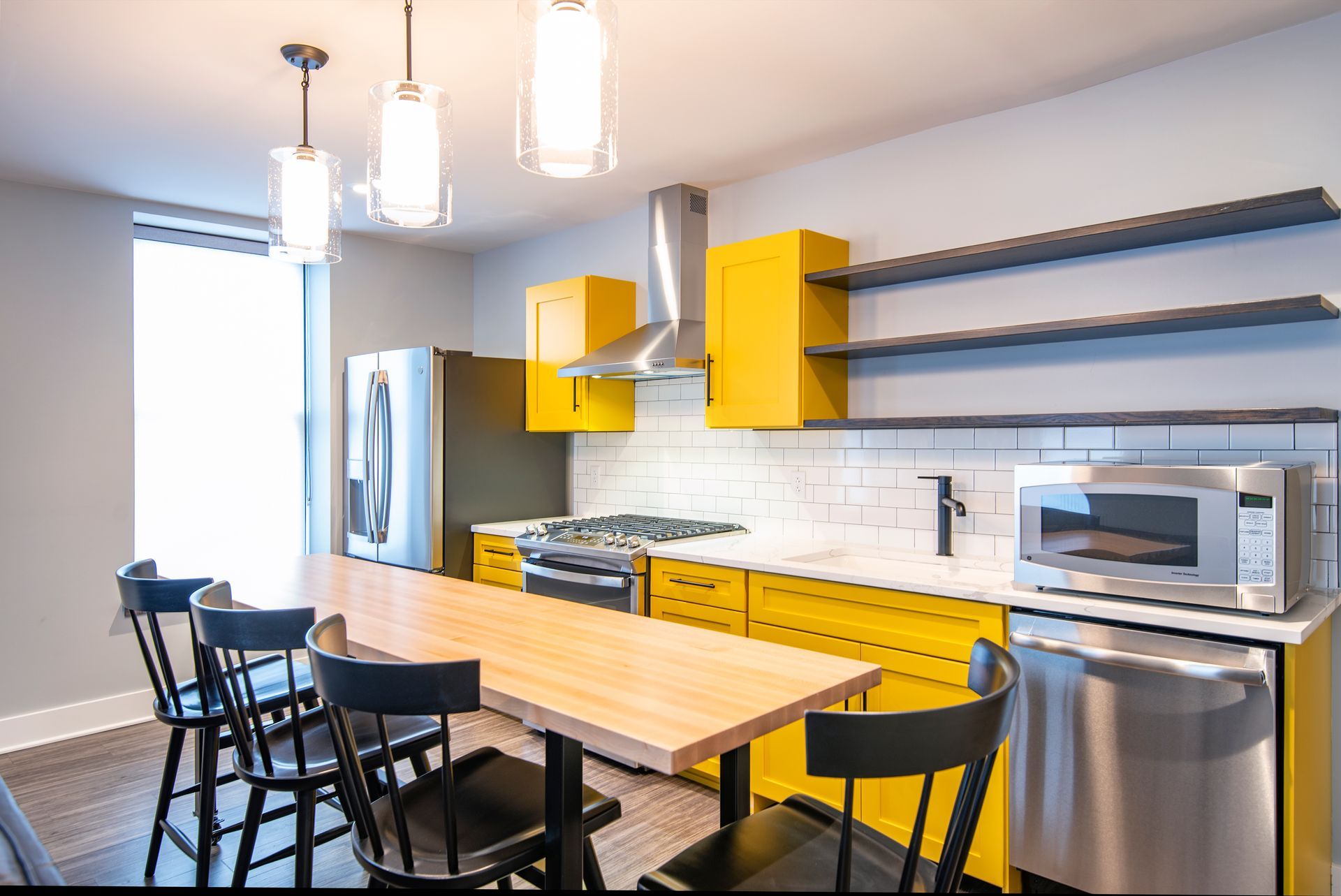 Modern kitchen with yellow cabinets, stainless appliances, and a wooden table with black chairs.