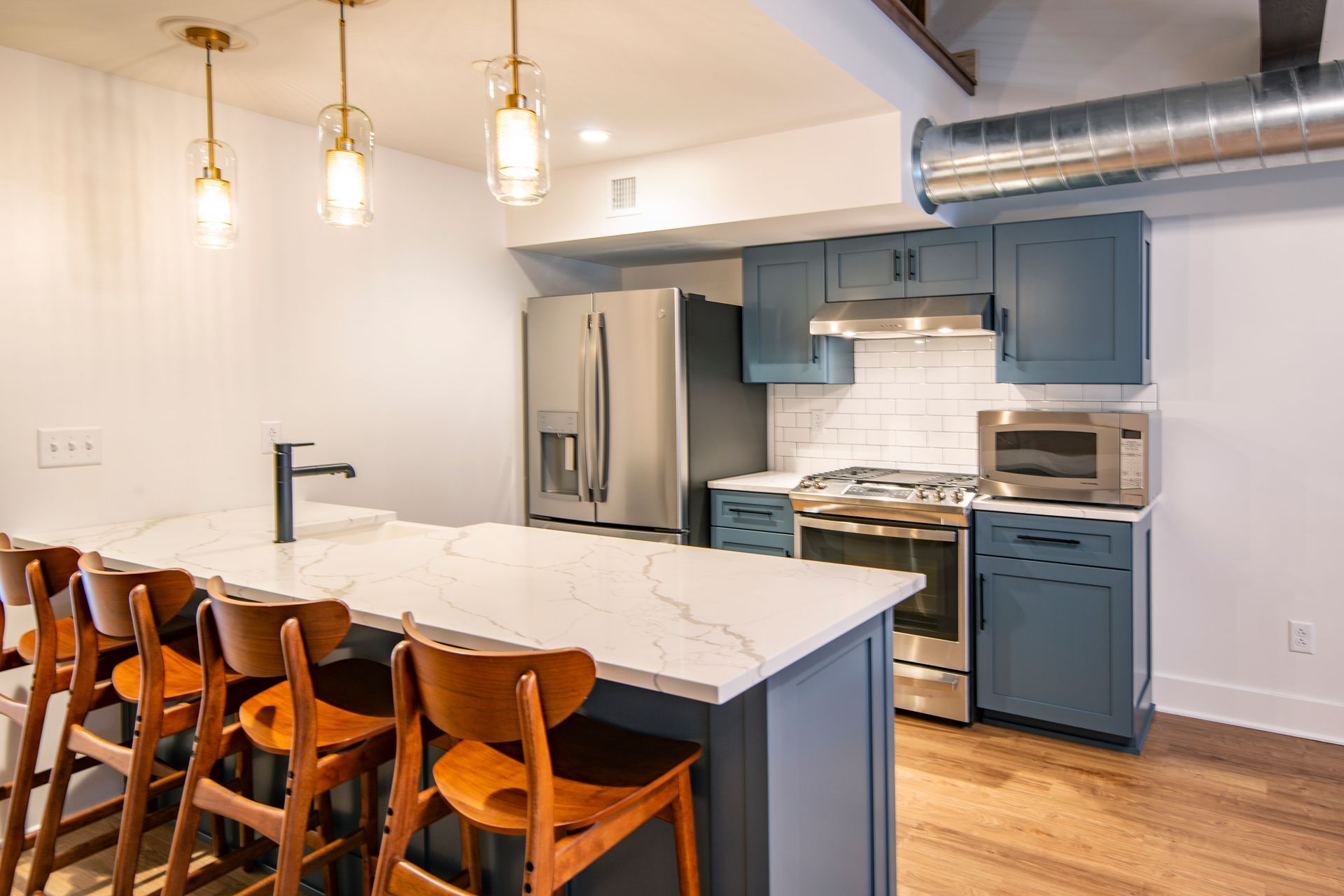 Modern kitchen with blue cabinets, stainless appliances, and a marble island with wooden stools.