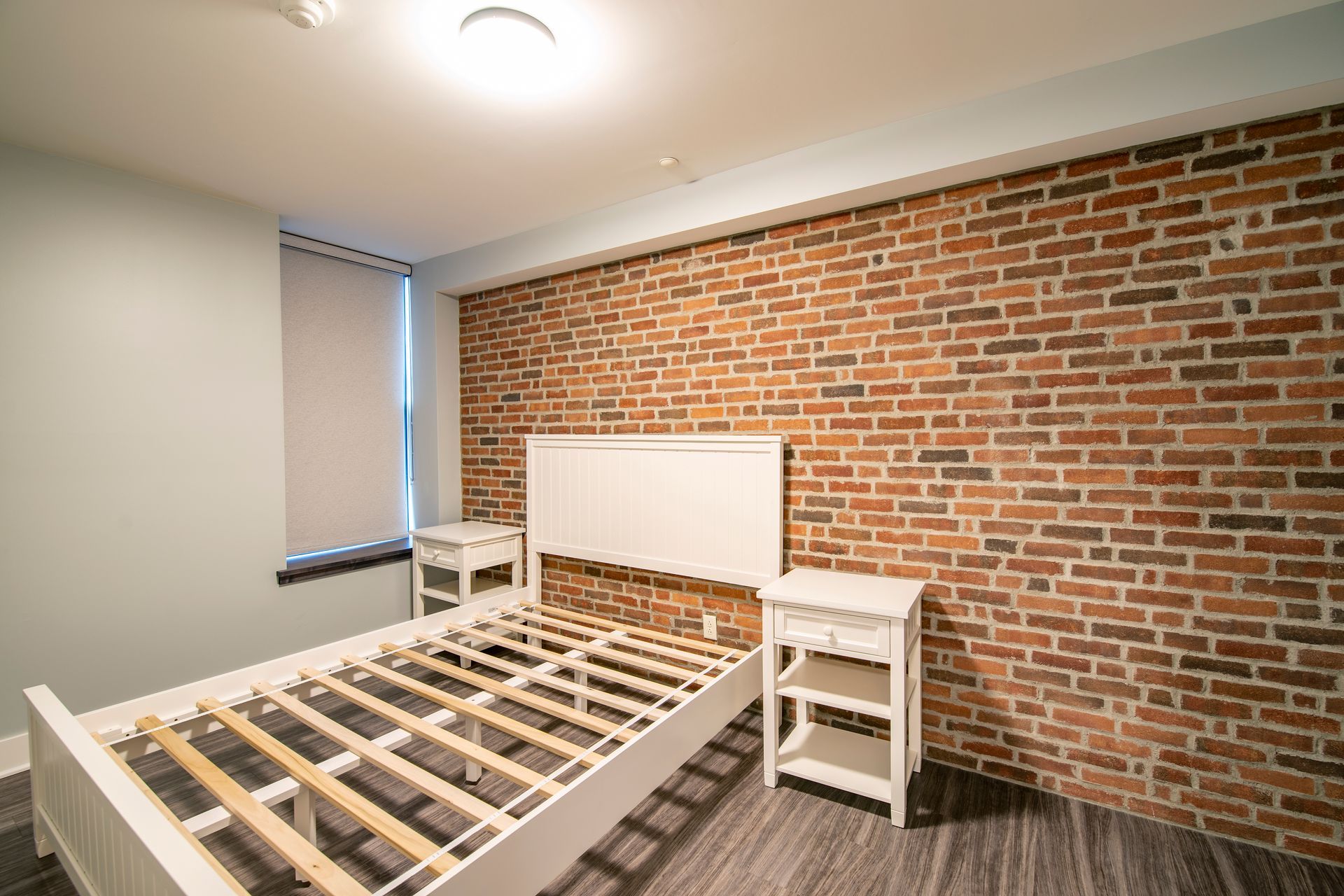 Modern bedroom with exposed brick wall and white bed frame under construction.