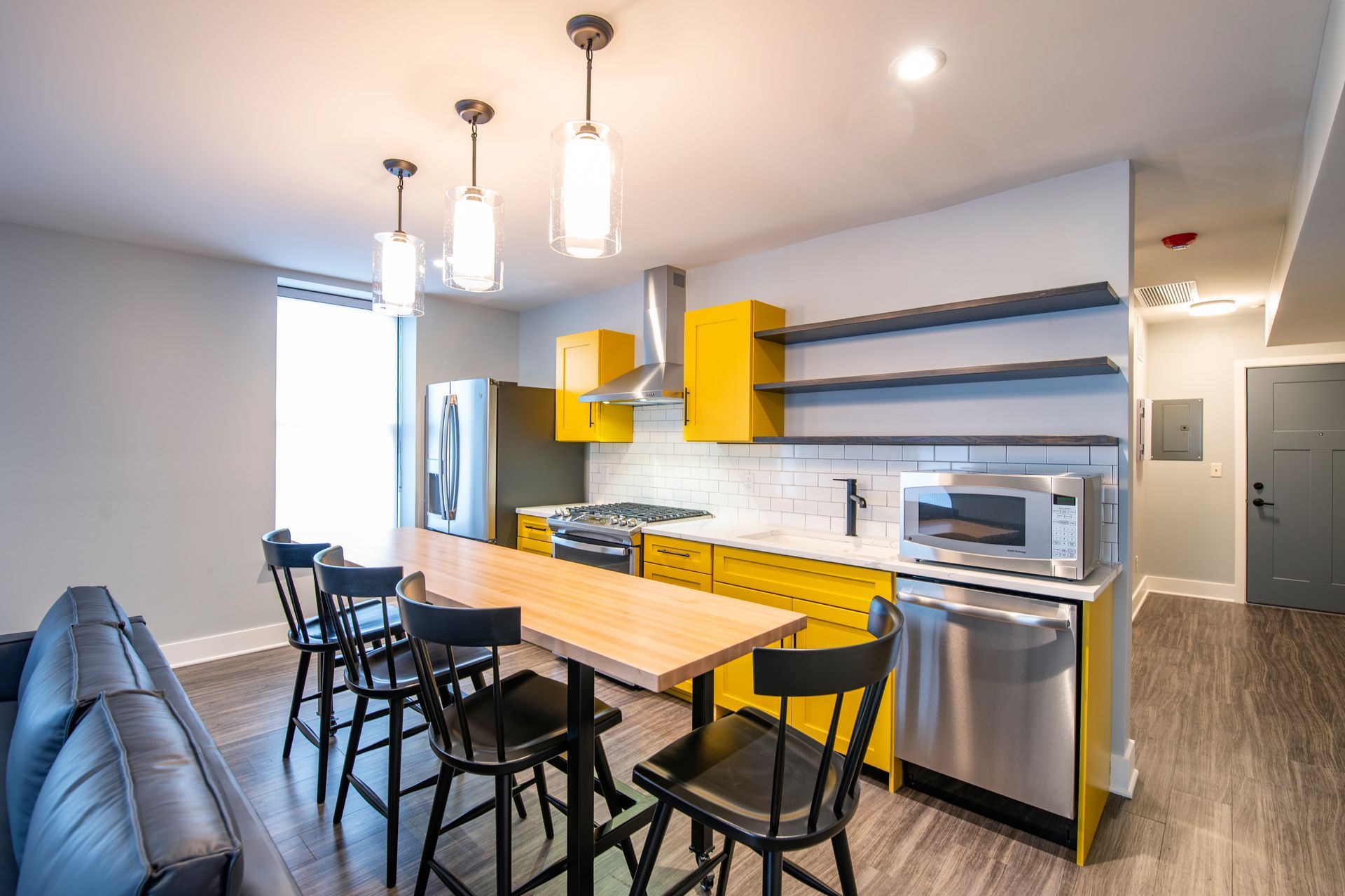 Modern kitchen with yellow cabinets, stainless appliances, island, and pendant lights.