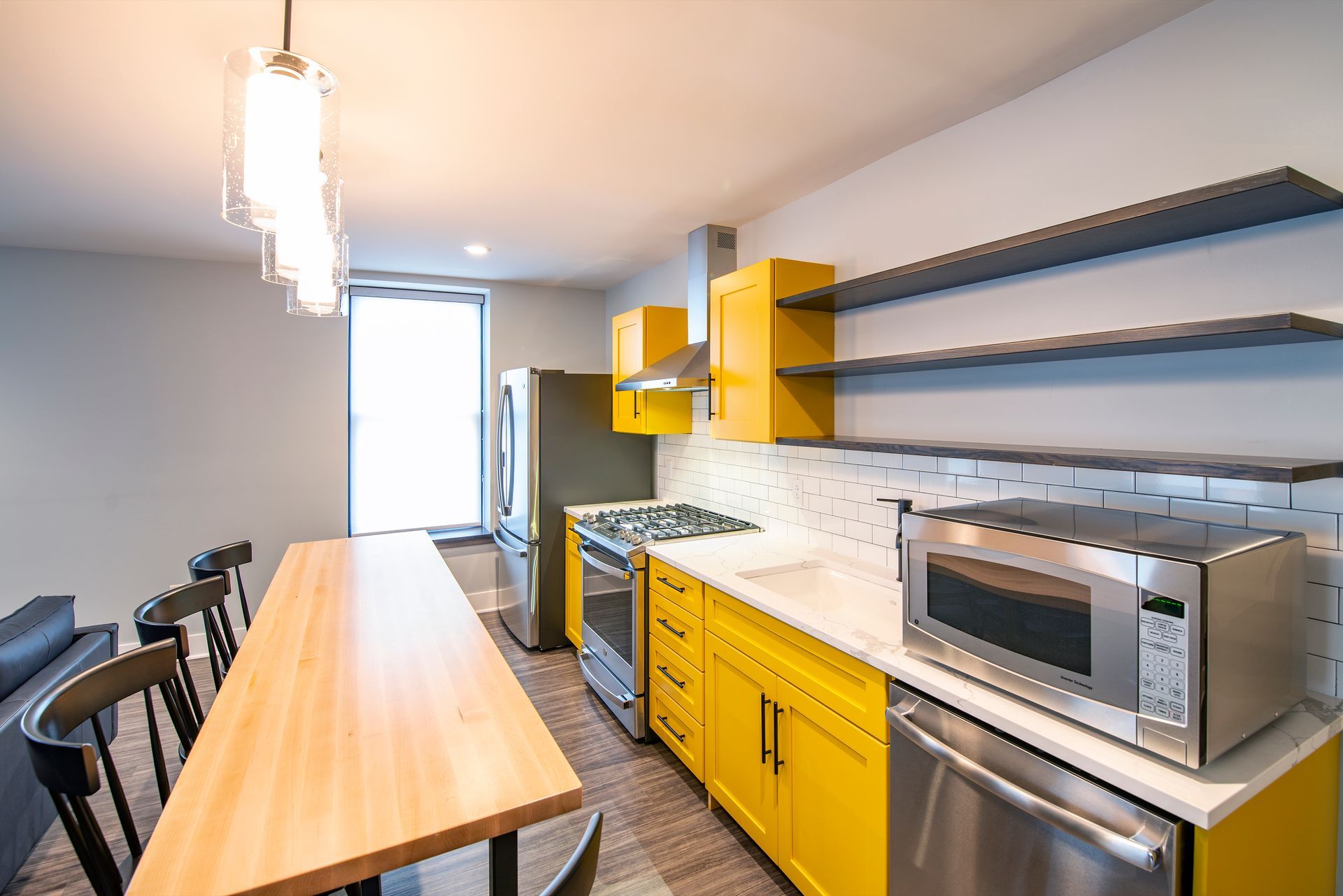 Modern kitchen with long wooden island, yellow cabinets, stainless appliances, and open shelving.