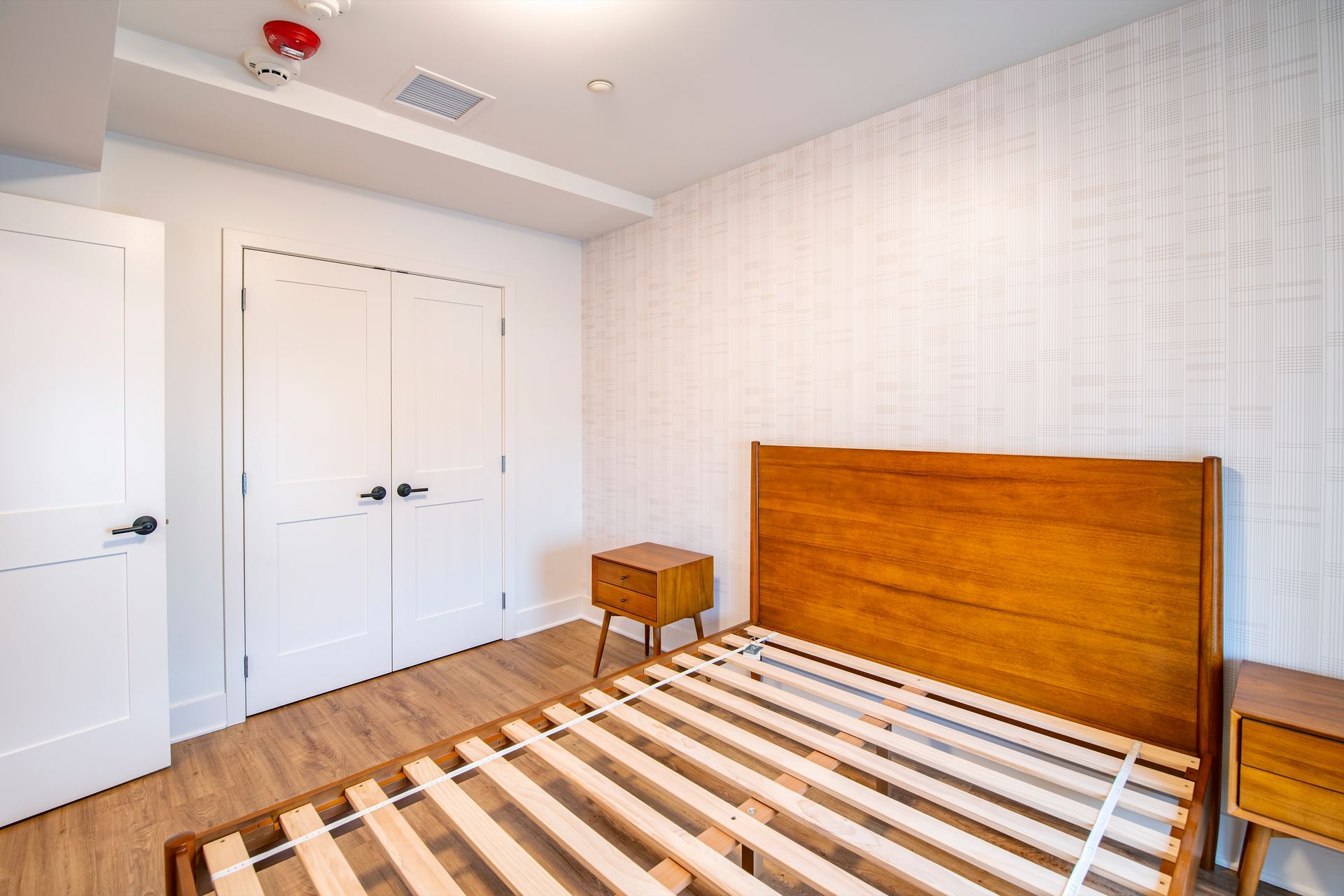 Bright bedroom with wooden bed frame, striped rug, white walls, and double closet doors.