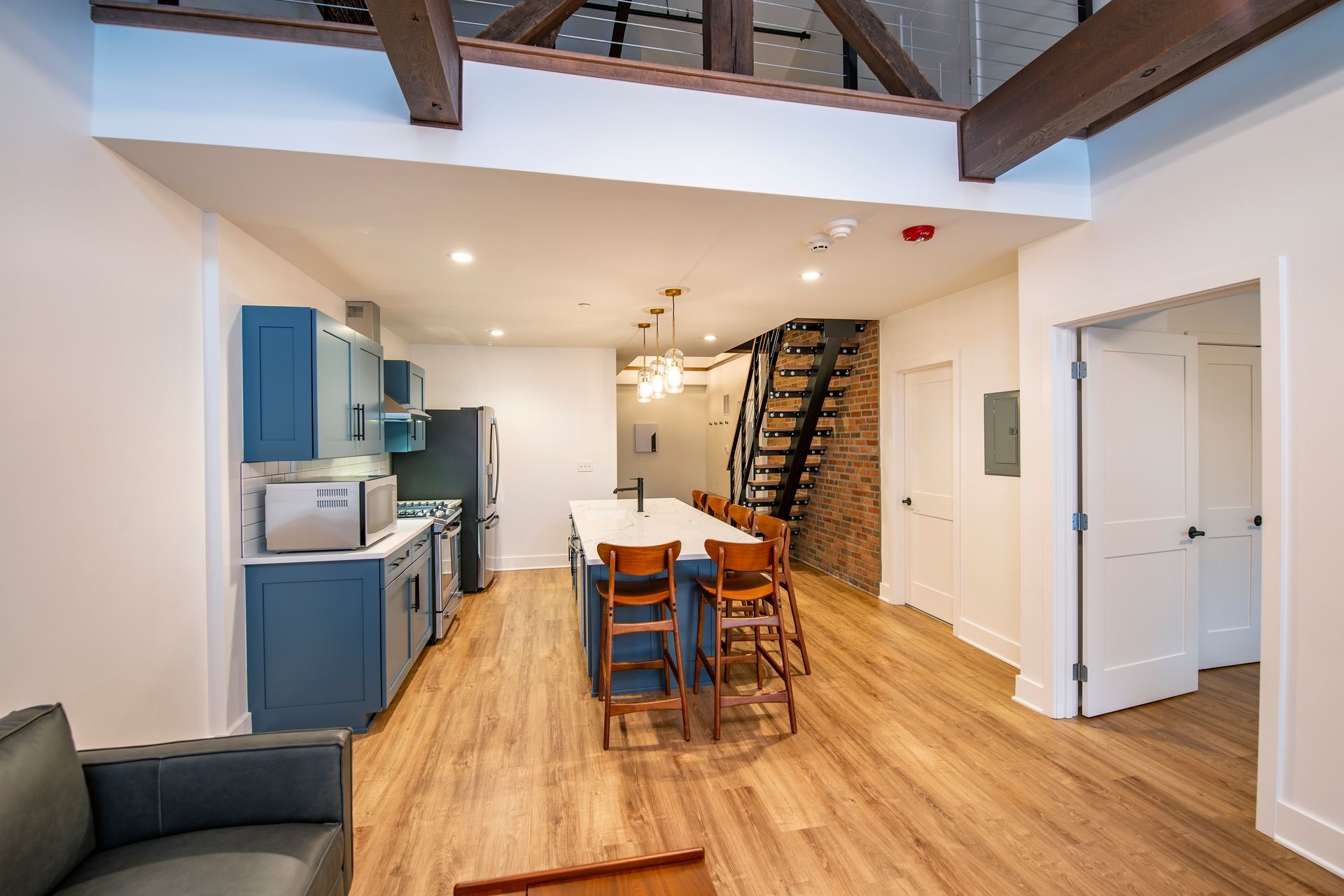 Open loft kitchen and dining area with blue cabinets, wood floors, exposed beams, and staircase.