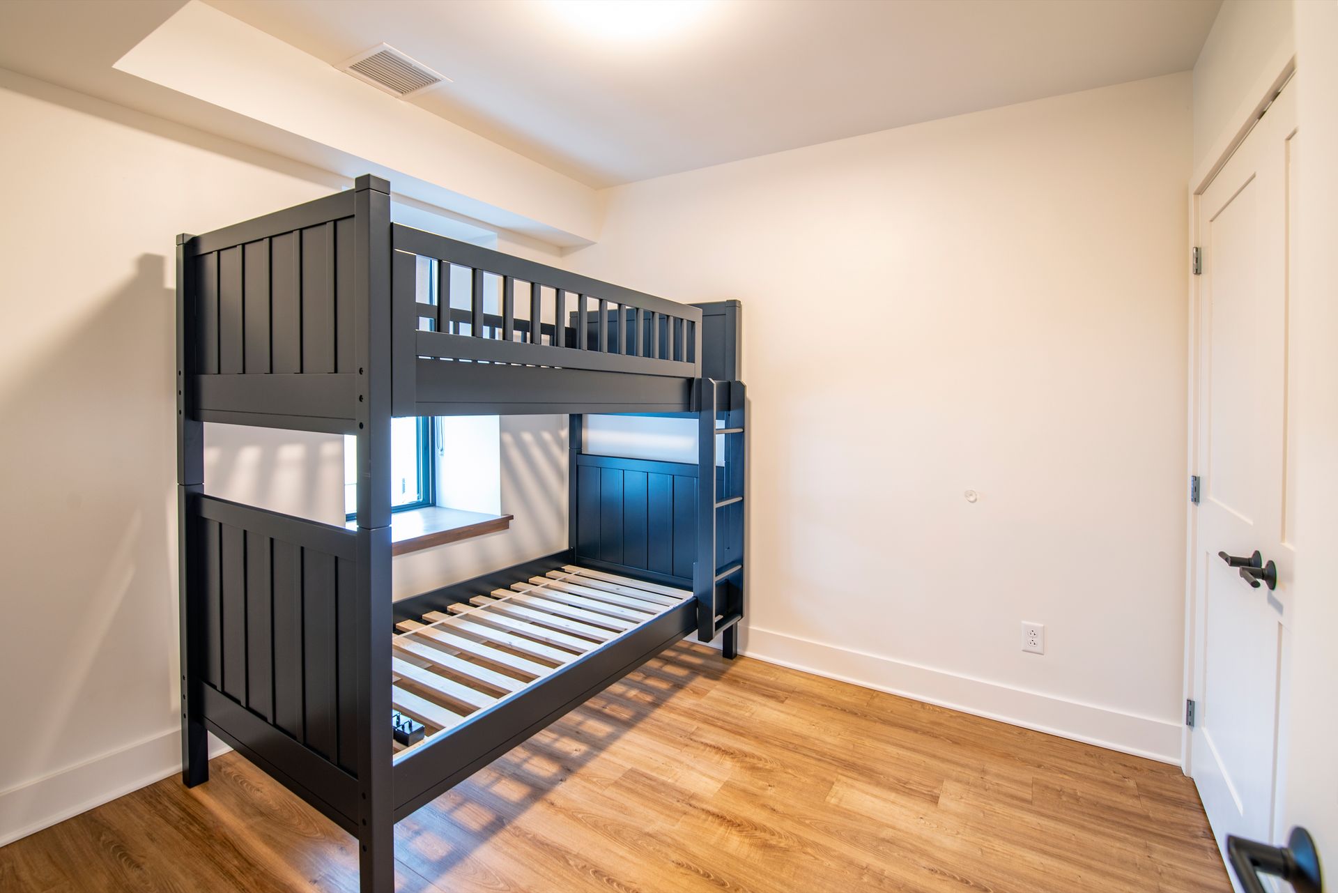 Modern room with black bunk bed, white walls, and hardwood floors.