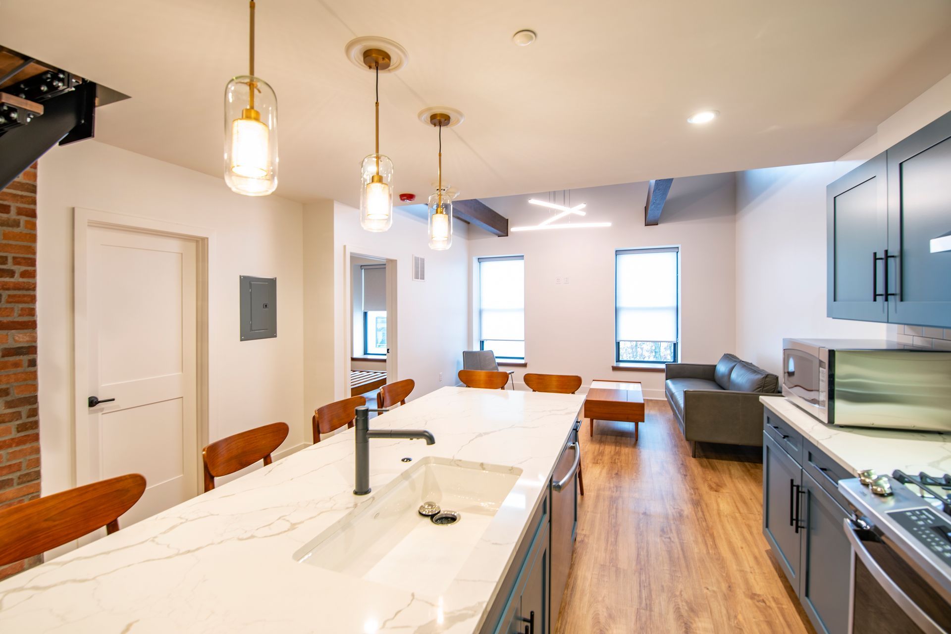 Modern kitchen with white island, wood floors, pendant lights, and stainless steel appliances.