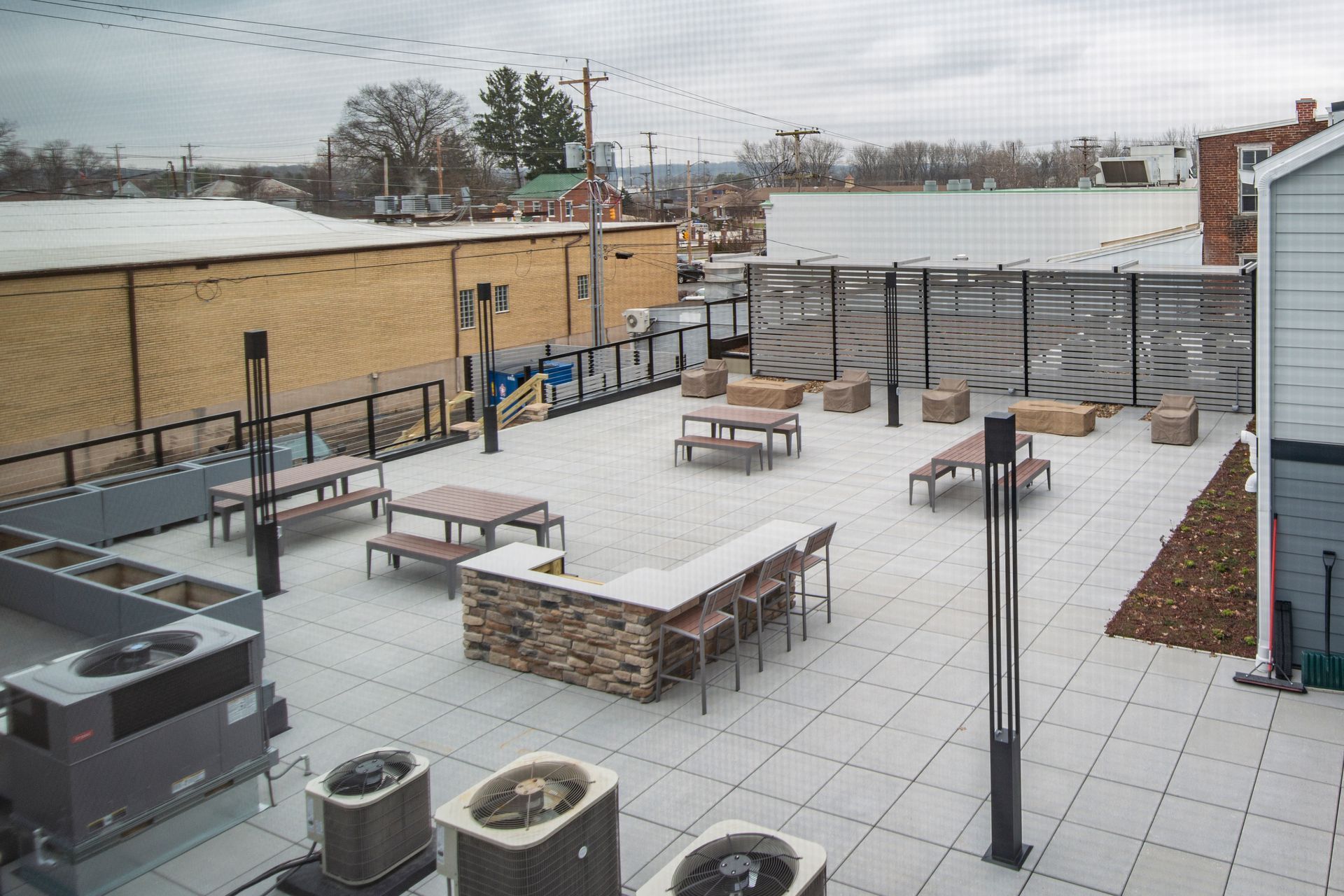 Outdoor rooftop patio with benches, tables, serving bar, and railings overlooking buildings.