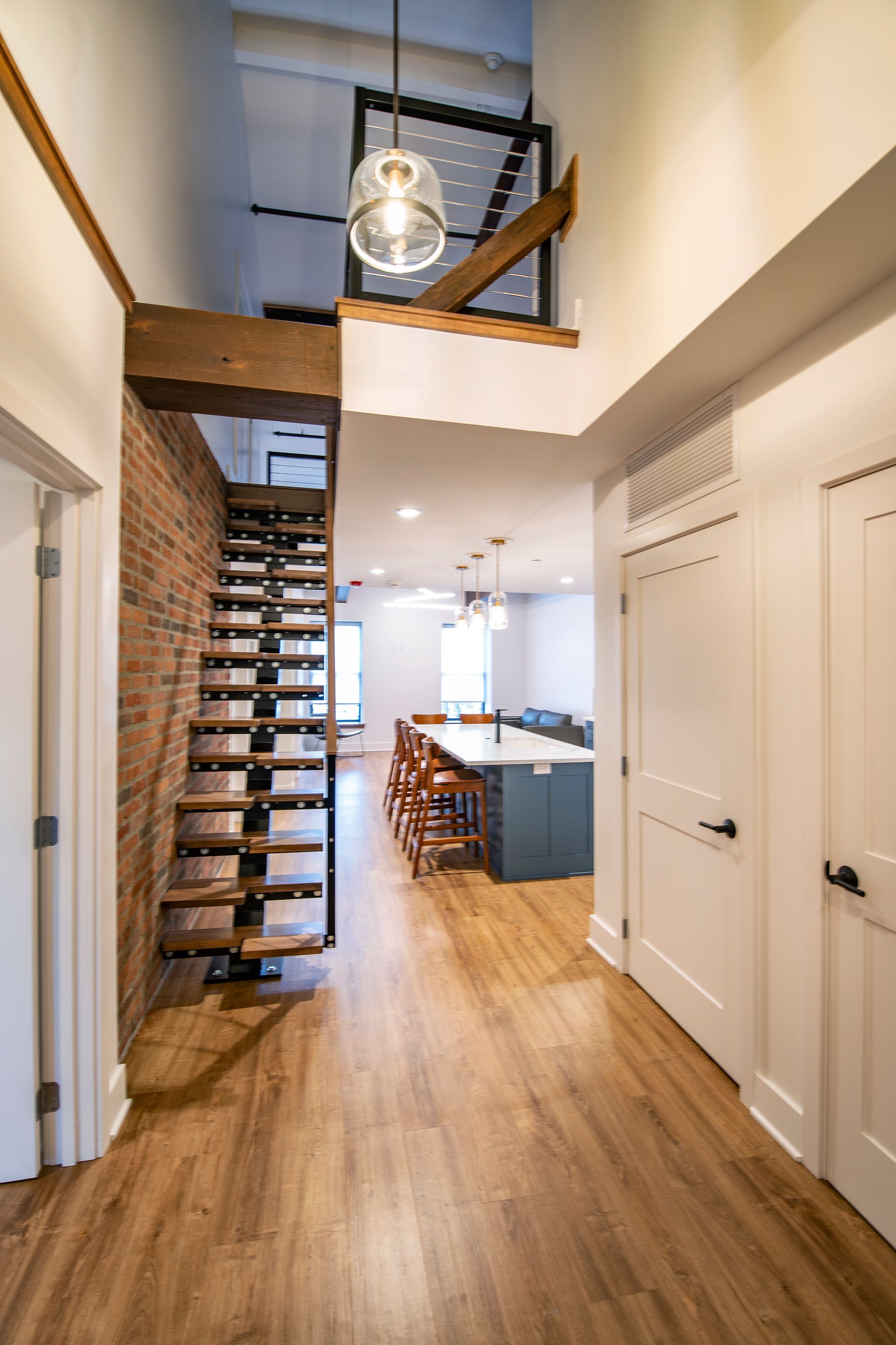 Modern hallway with wood floors, open stairs, and a kitchen visible in the background.
