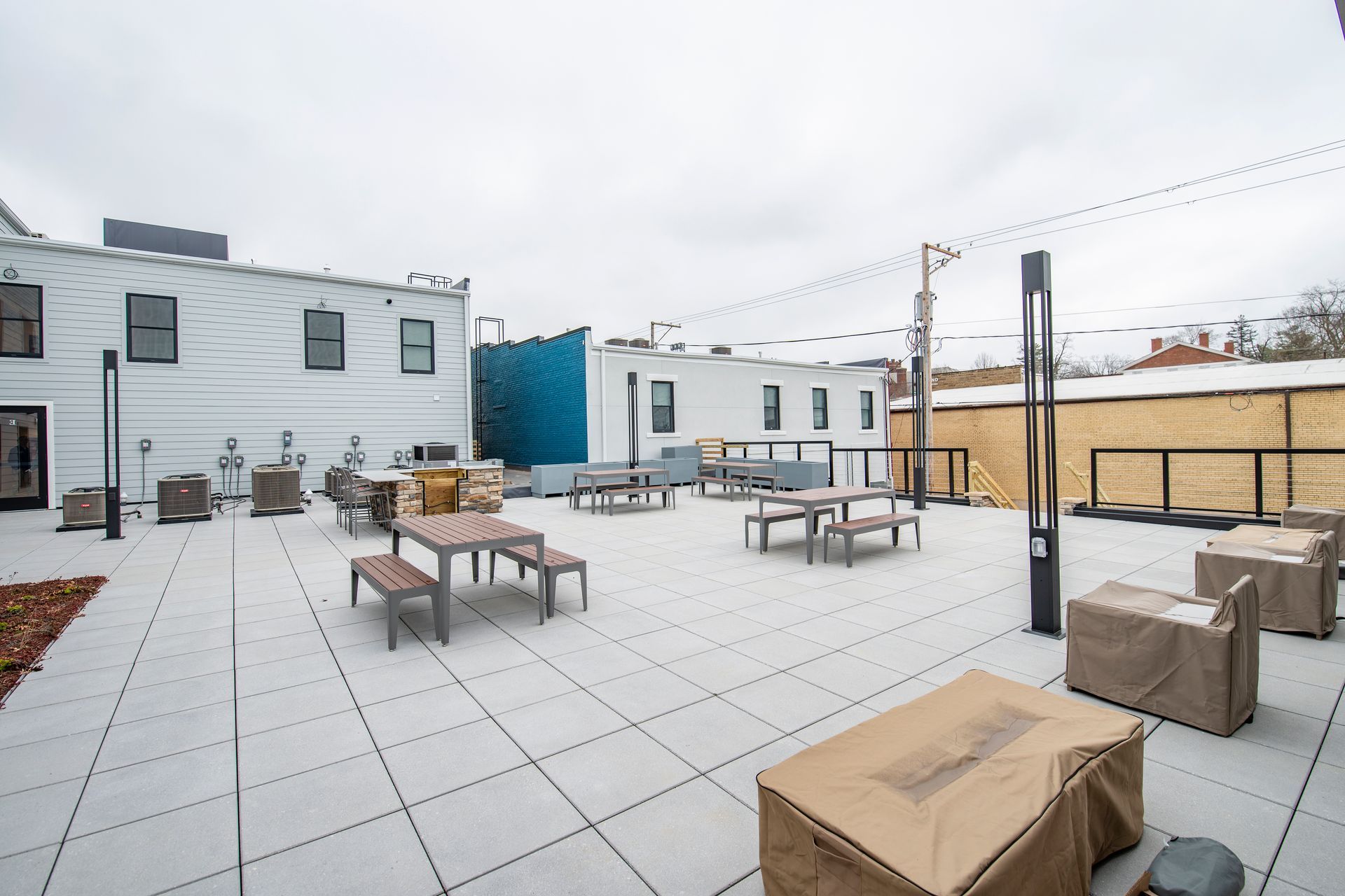Outdoor rooftop patio with tables, benches, string lights, and covered seating on a cloudy day.