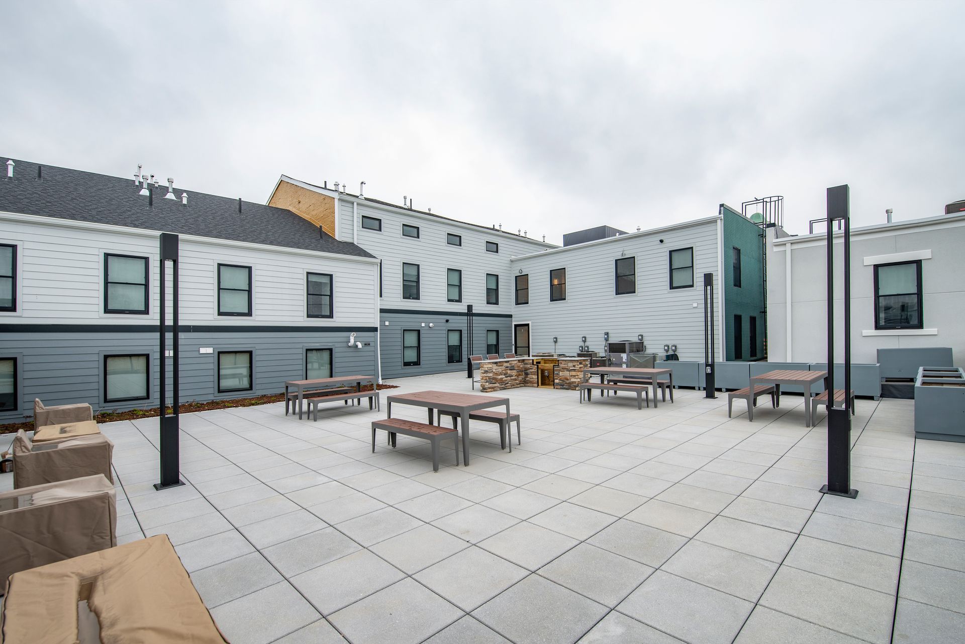 Outdoor rooftop patio with tables and benches beside modern white buildings.