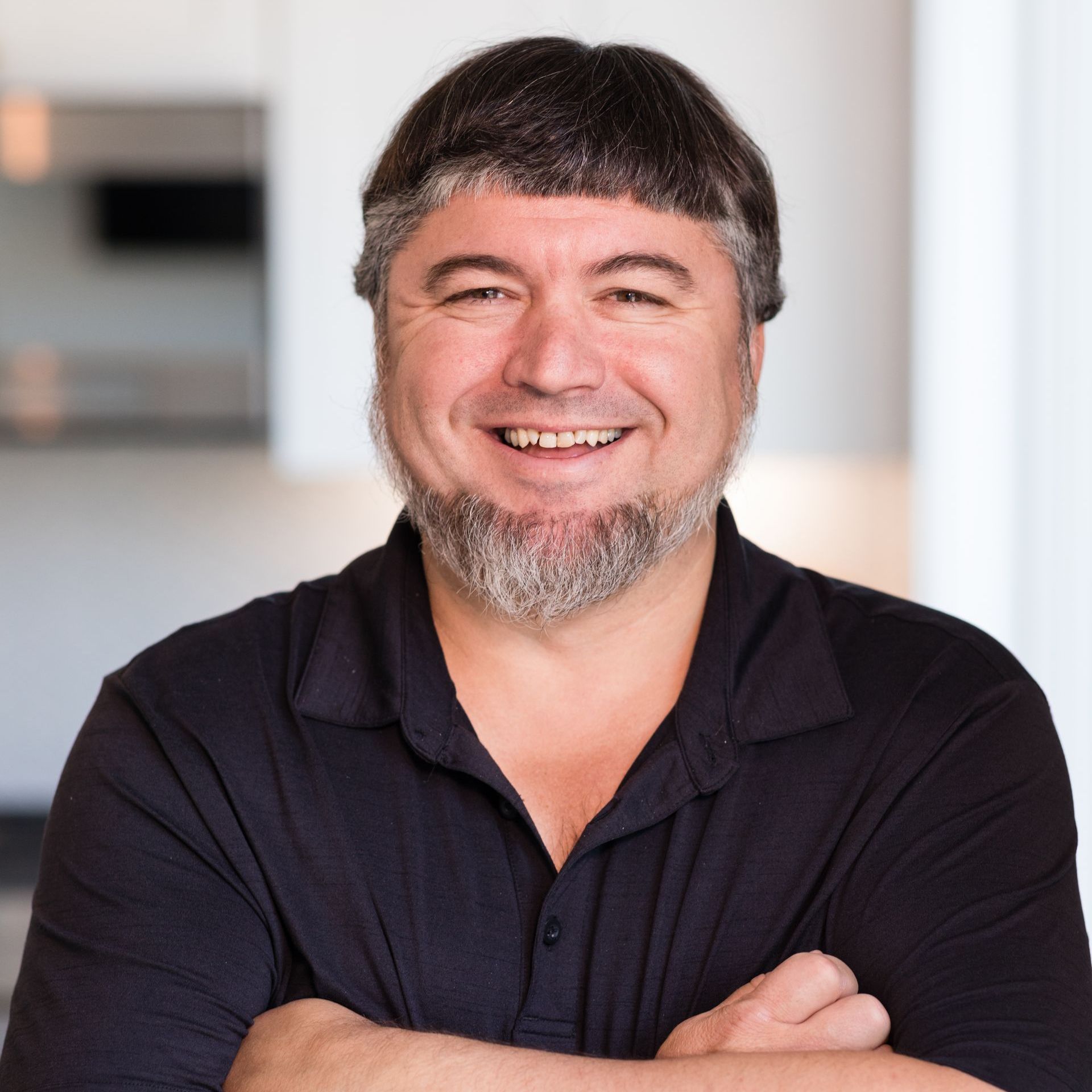 A man with a beard is smiling with his arms crossed.