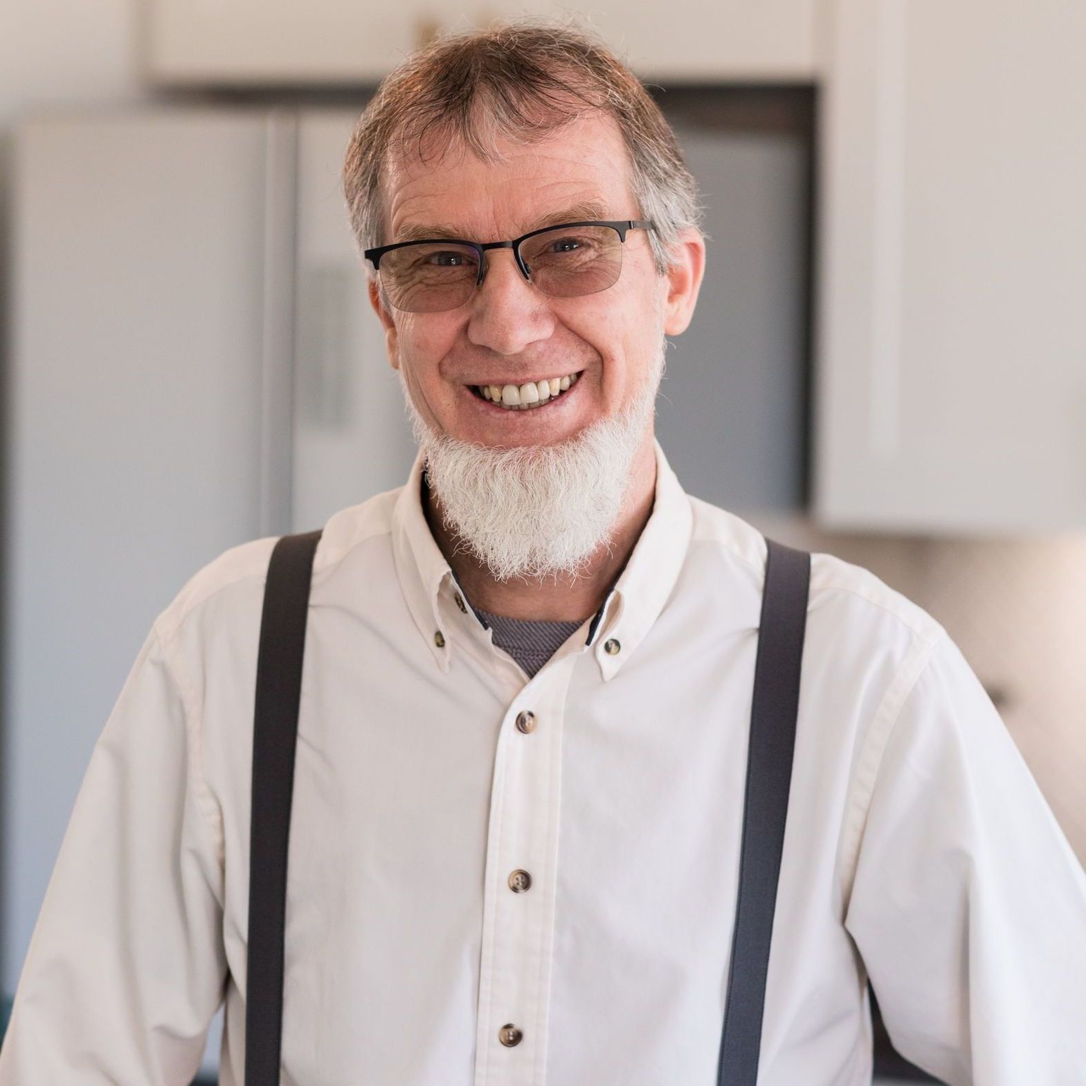 A man with a beard and suspenders is smiling for the camera.