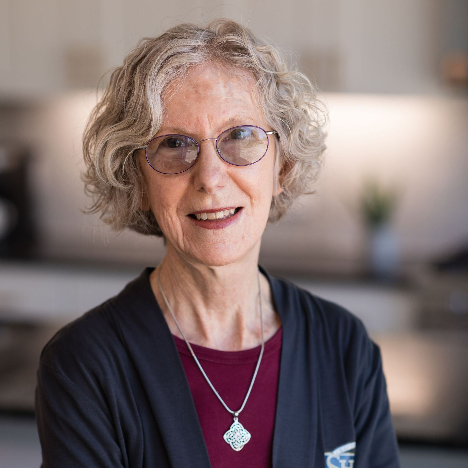 A woman wearing glasses and a necklace is smiling for the camera.