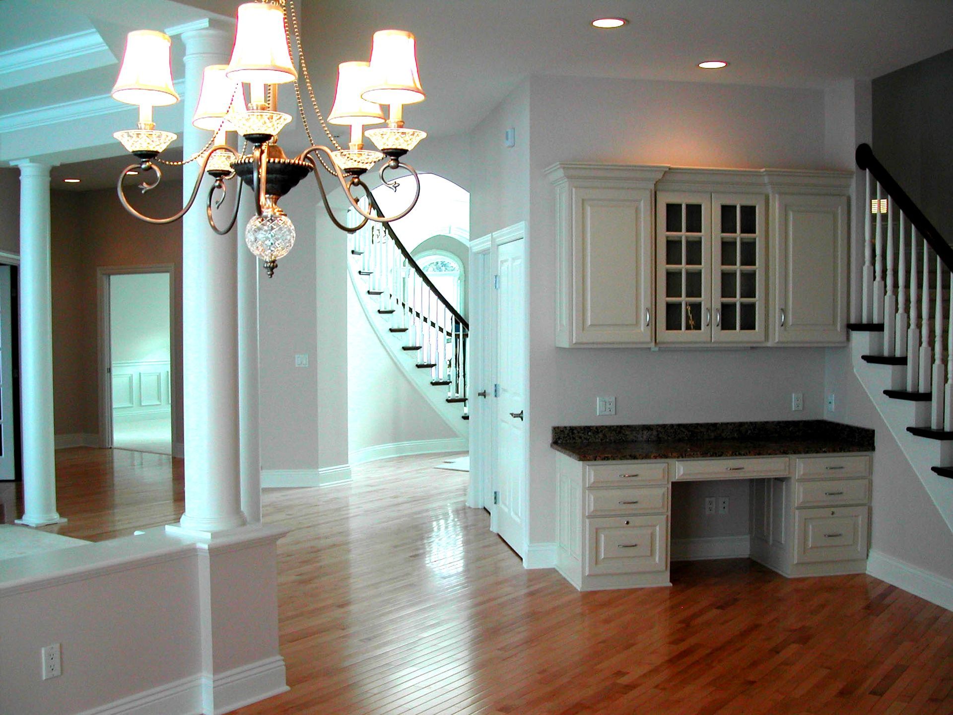 An empty room with a desk and stairs and a chandelier hanging from the ceiling.