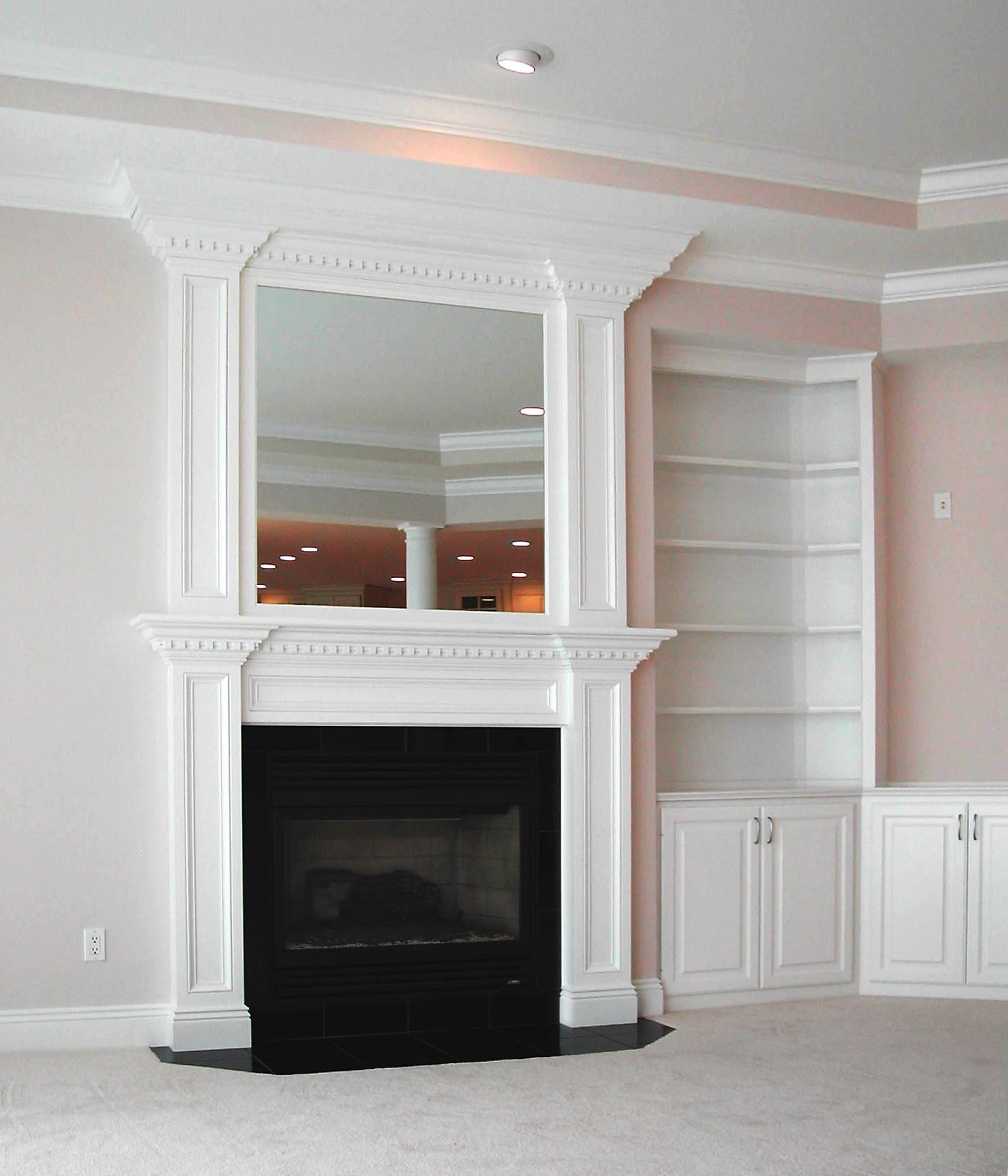 An empty living room with a fireplace, a mirror, and shelving.