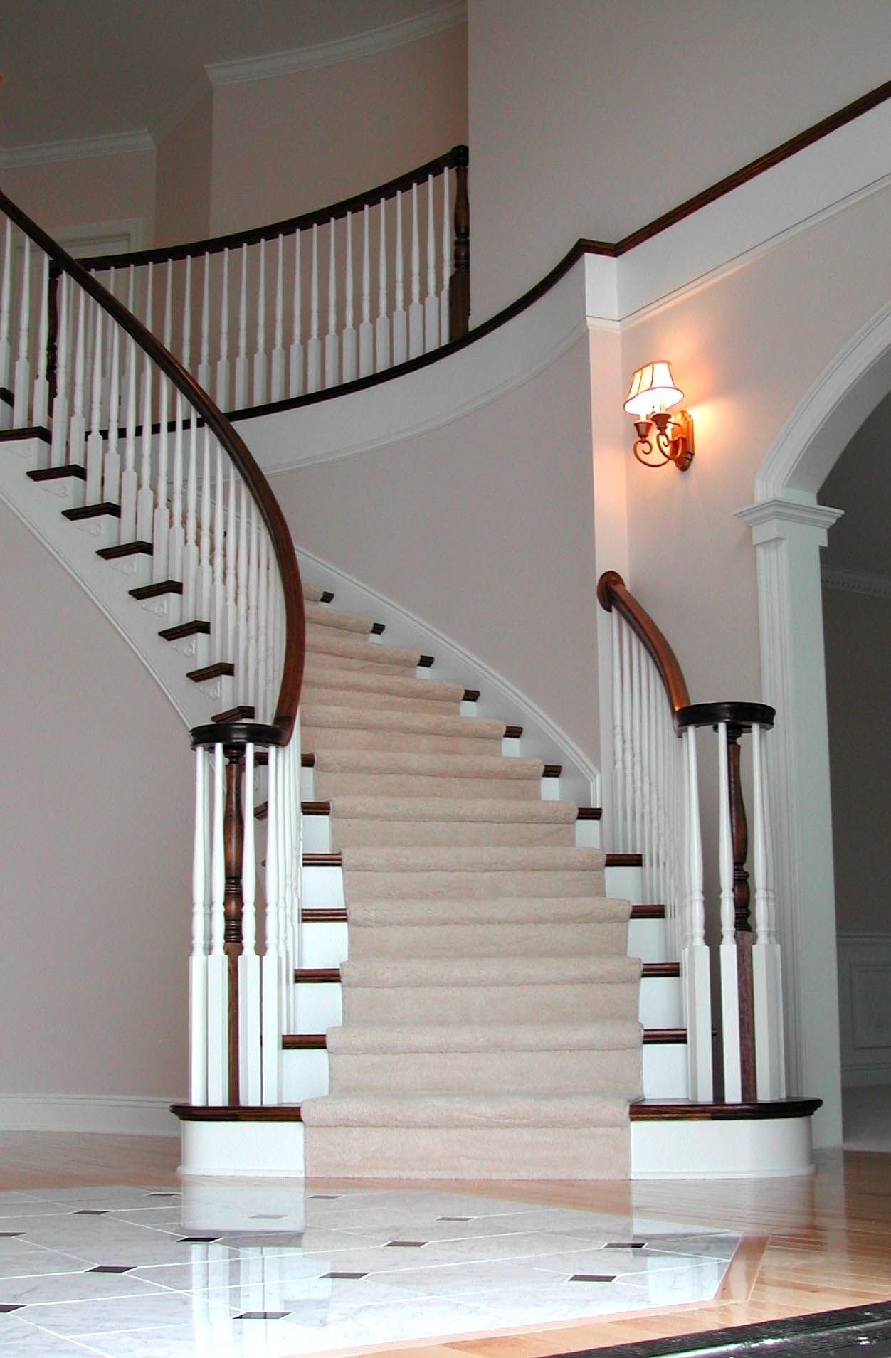A curved staircase with white railings and a light on the wall.