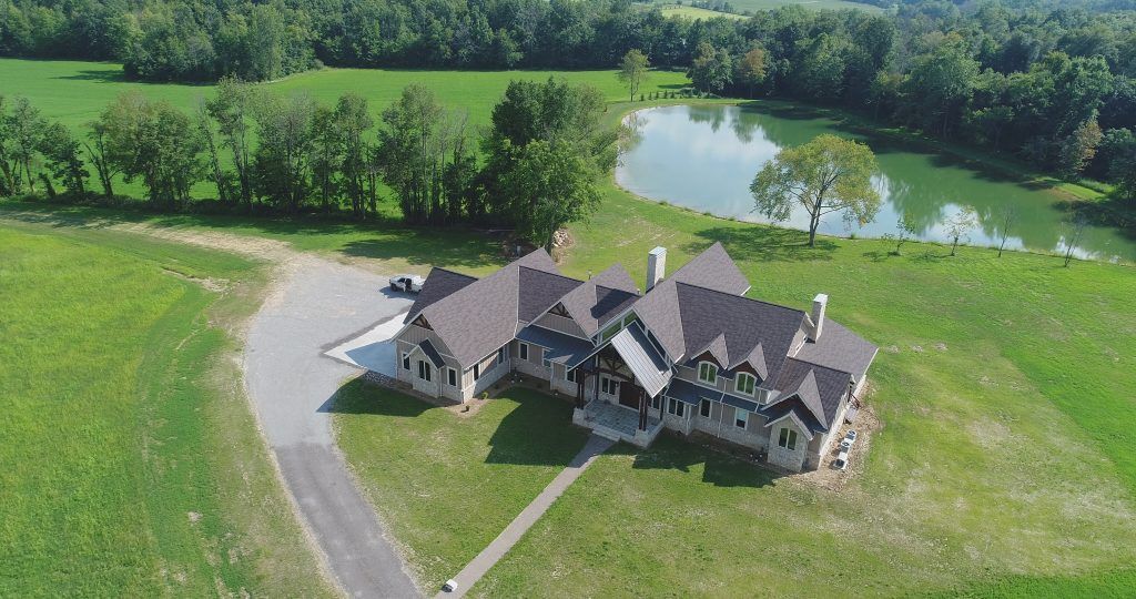 An aerial view of a large house with a pond in the background.