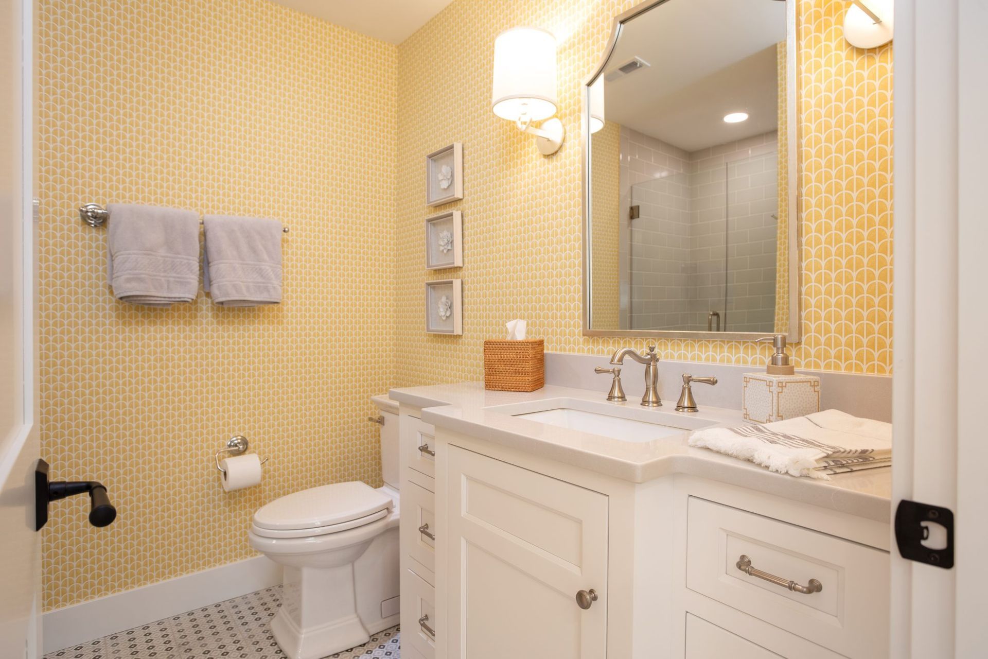 A bathroom with a toilet, sink, mirror and yellow wallpaper.