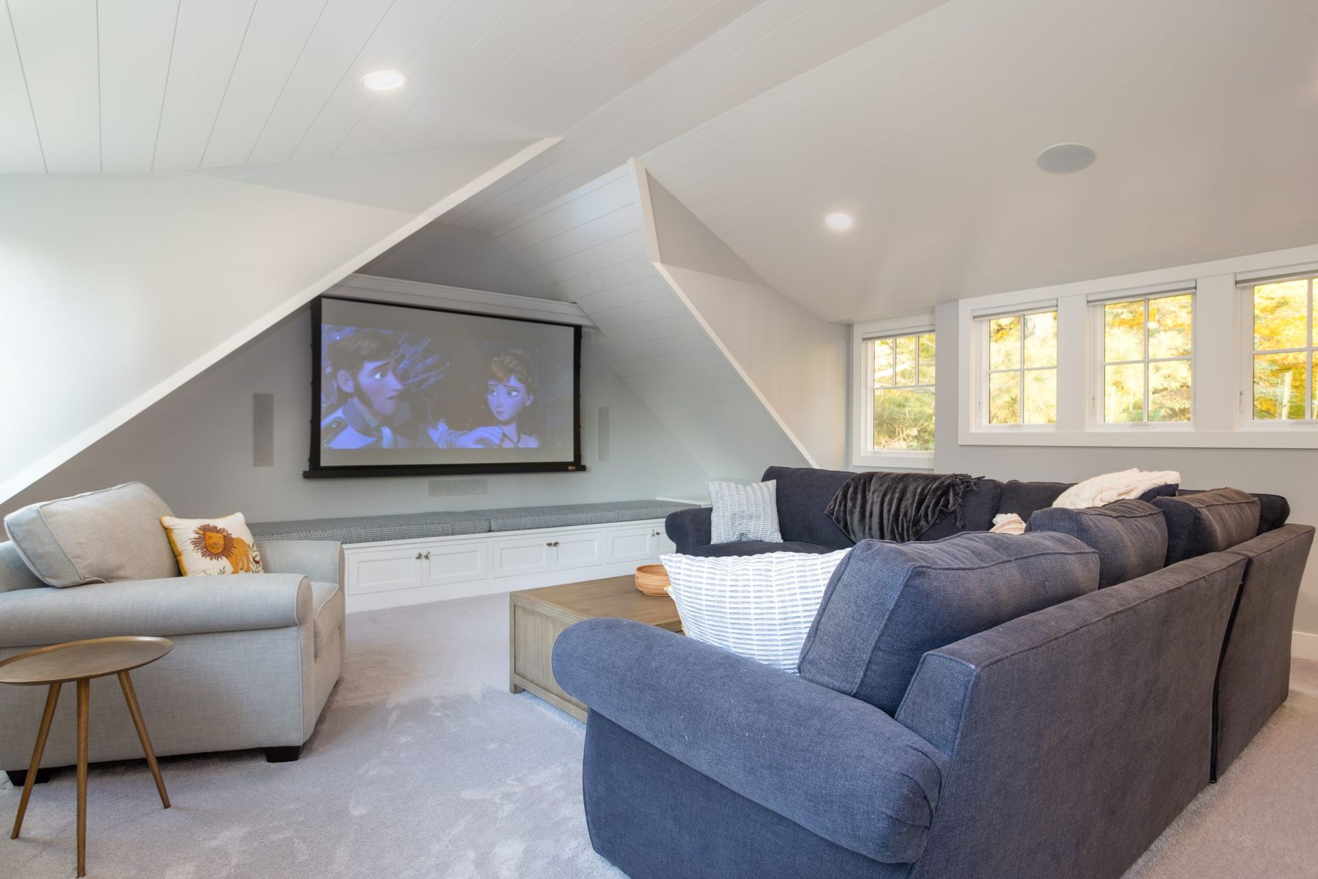 A living room with a large sectional couch and a projector screen.