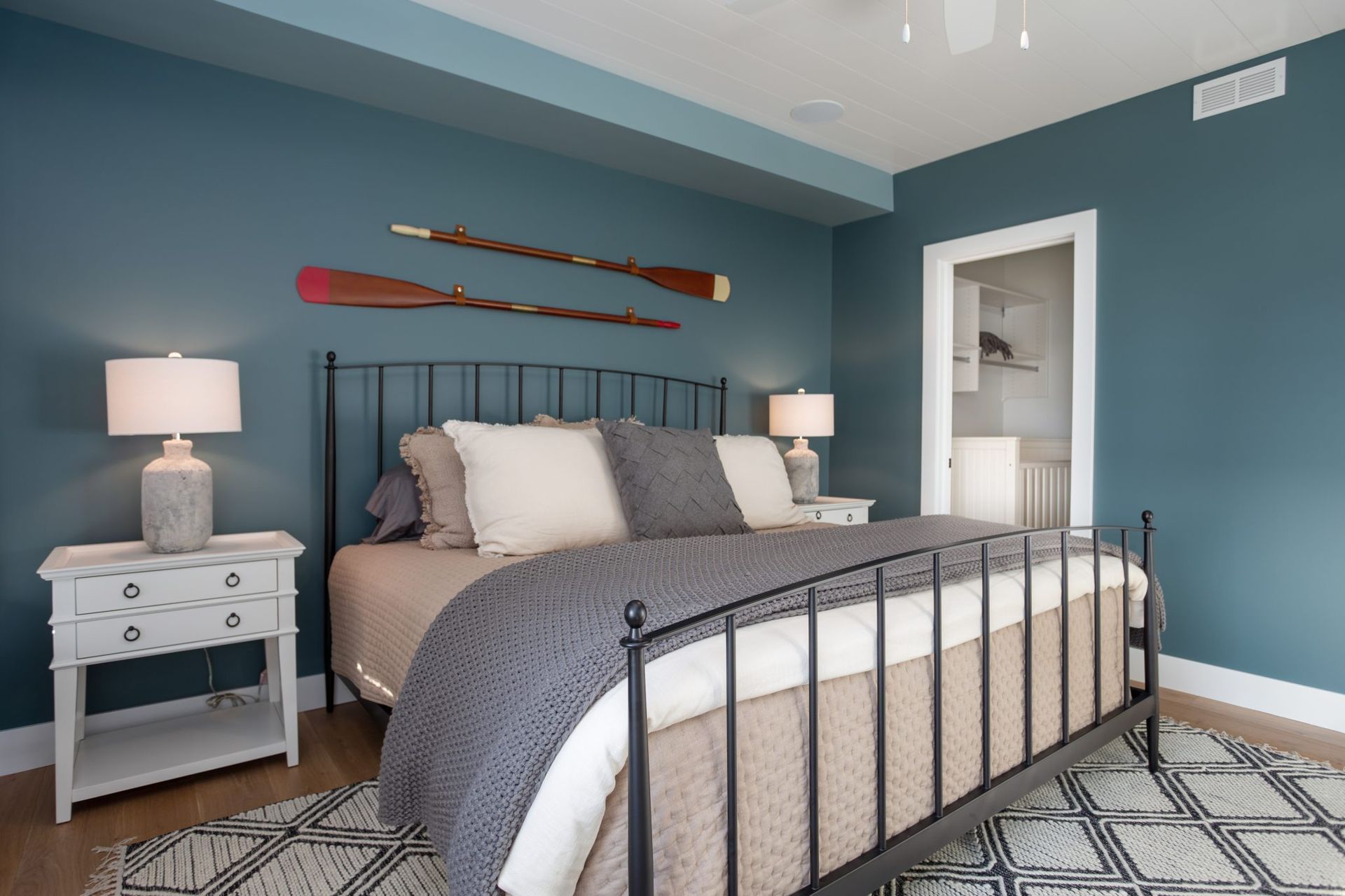 A bedroom with a bed, nightstands, lamps, and oars hanging on the wall.