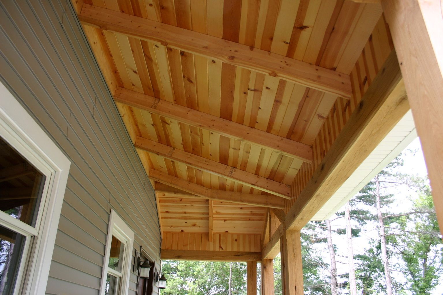 A porch with a wooden roof and a gray house in the background.