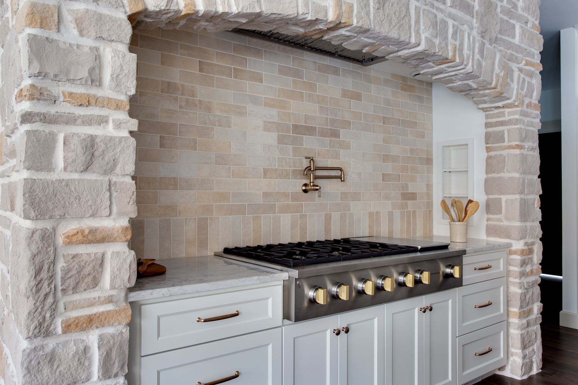 A kitchen with a stove top oven and a stone wall.