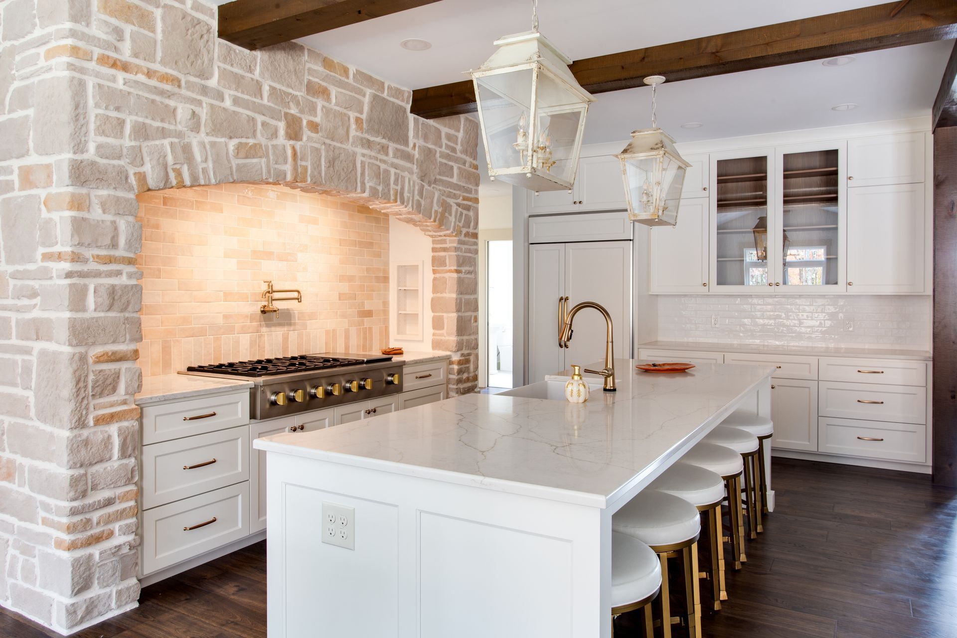 Bright white kitchen with stone accents, large island, brass fixtures, and hanging pendant lights.