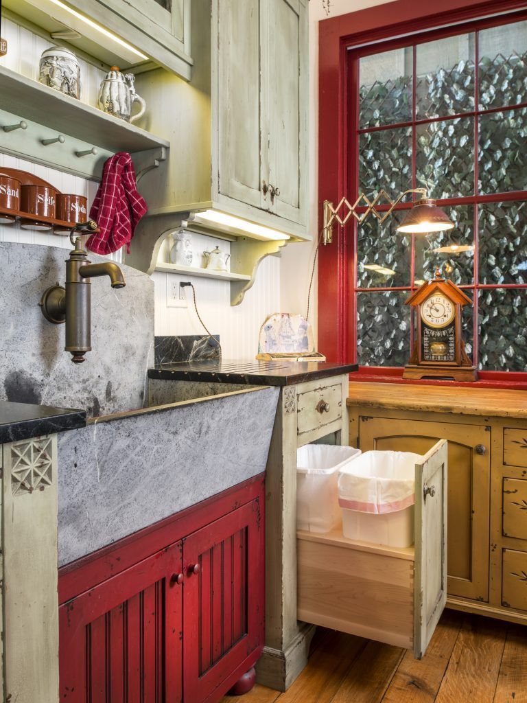 A kitchen with a sink and a trash can in the drawer.