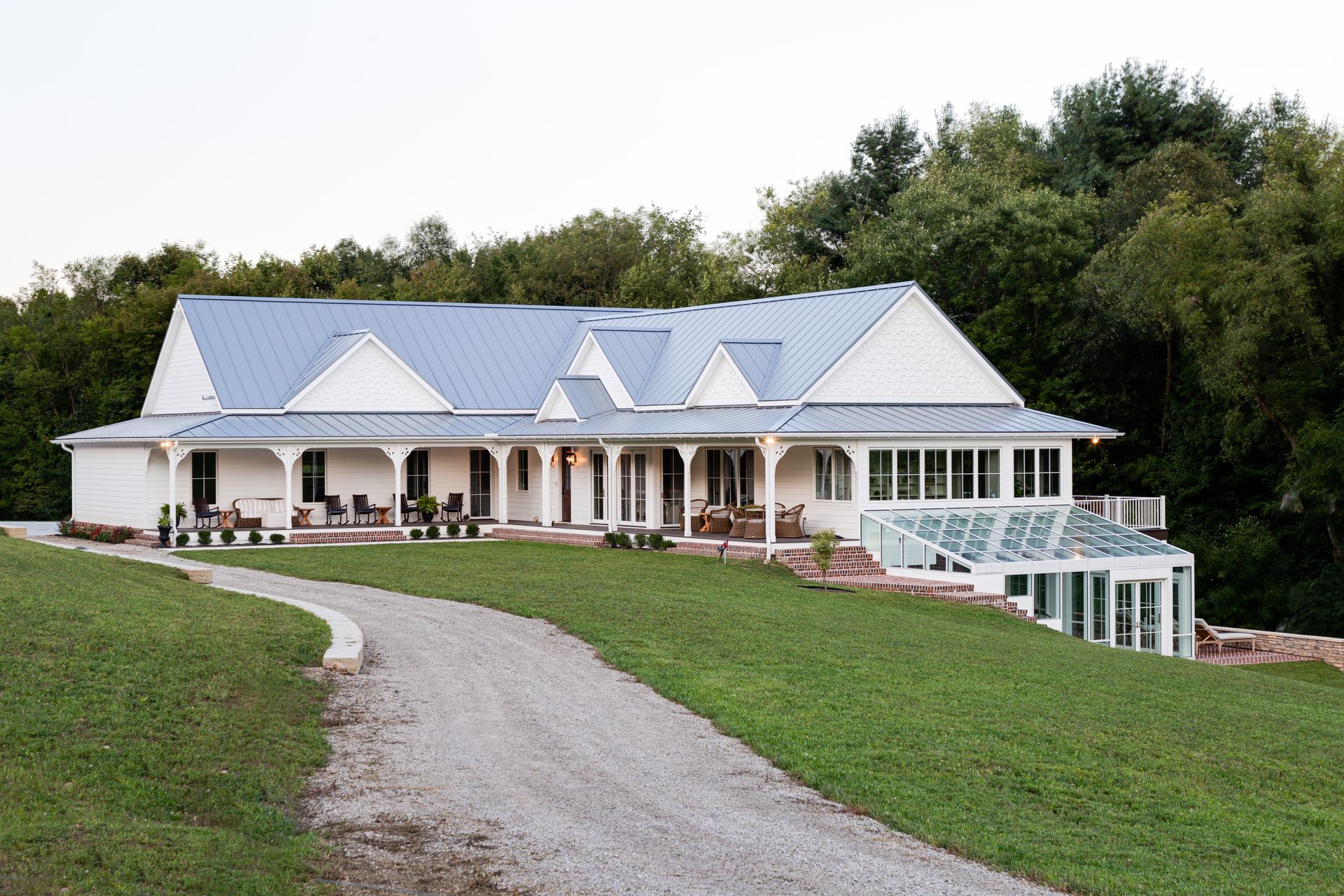 A white house with a blue roof and a gravel driveway leading to it.