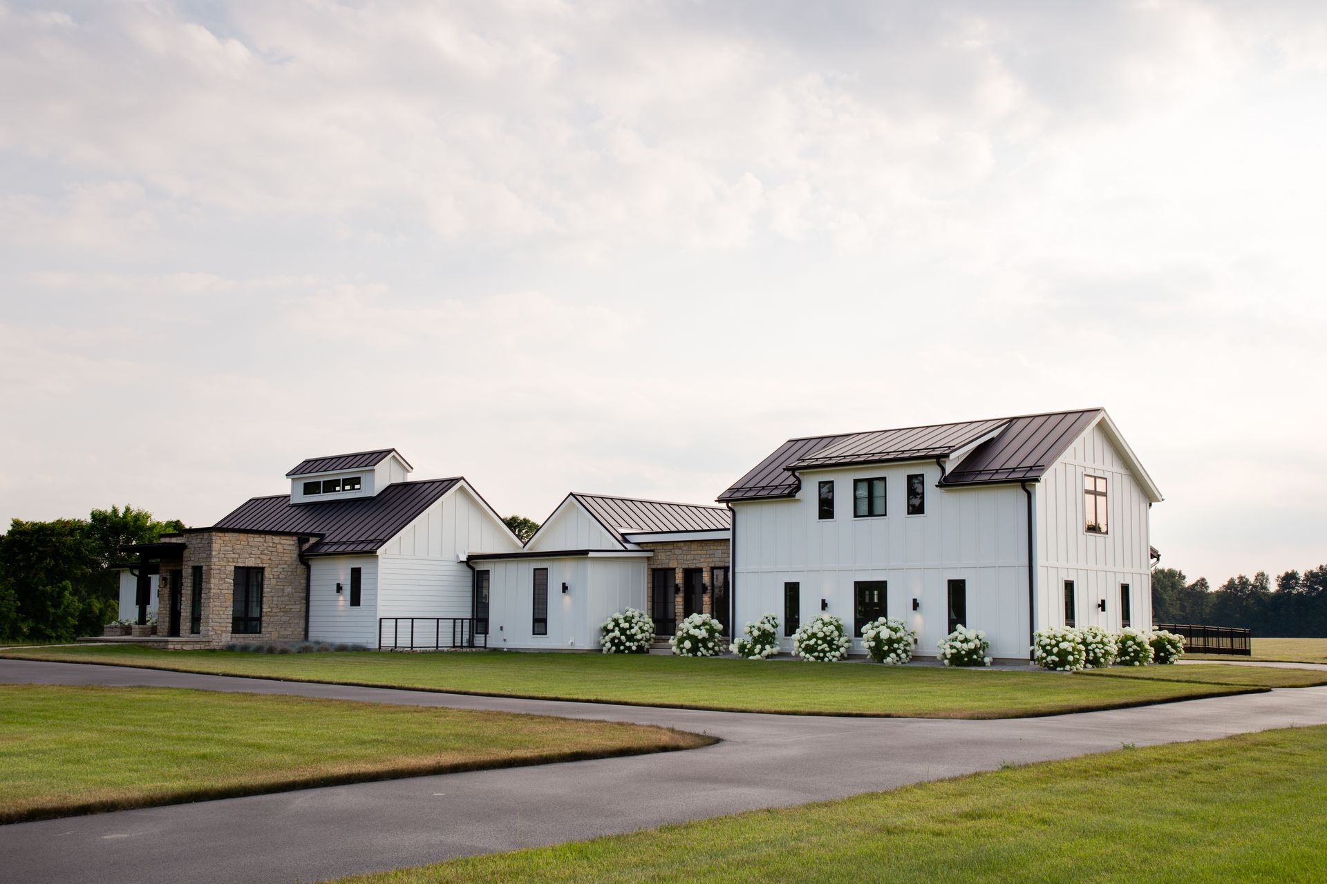 A large white house with a black roof is sitting on top of a lush green field.