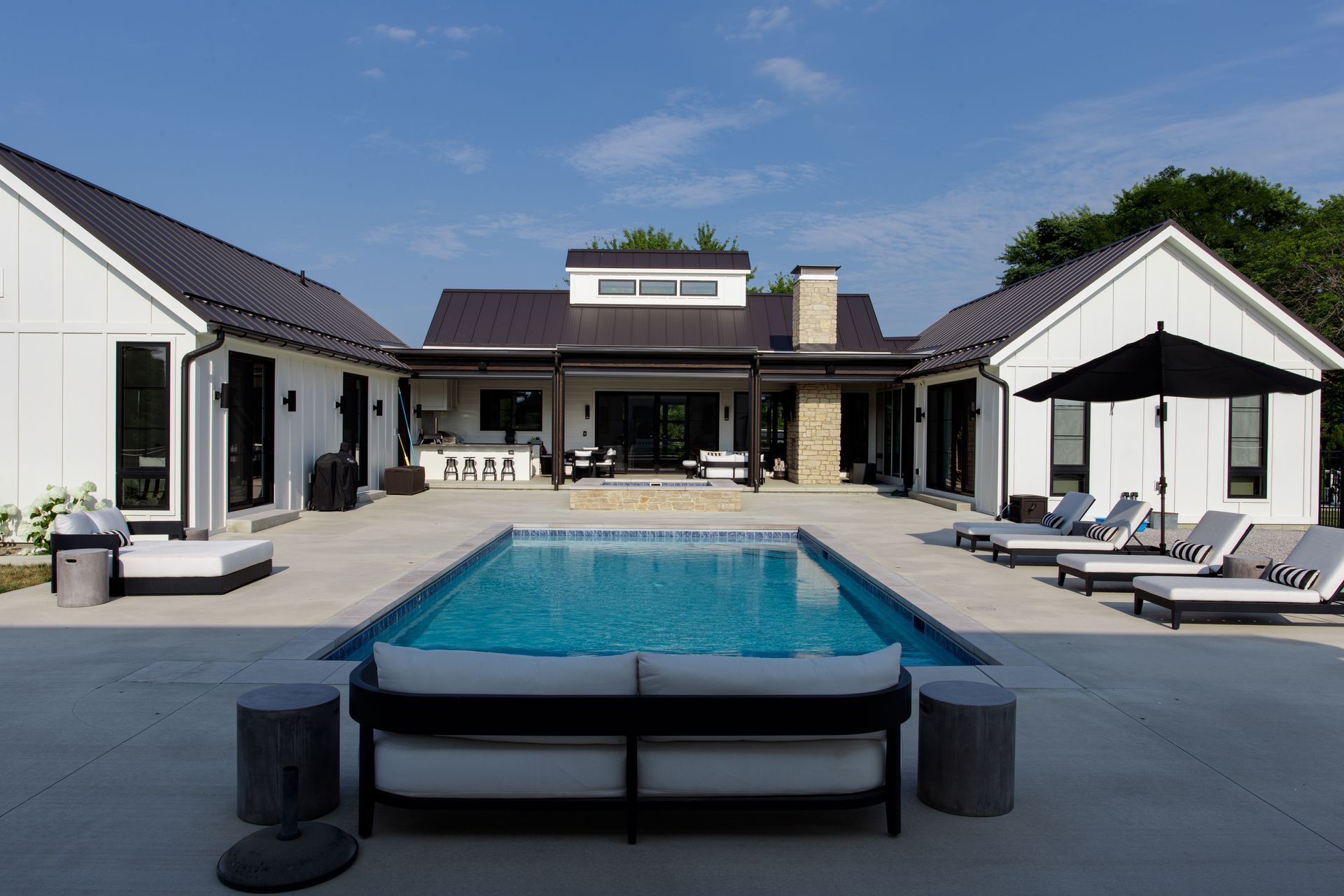 Modern backyard patio with a swimming pool, lounge chairs, and a contemporary white house.