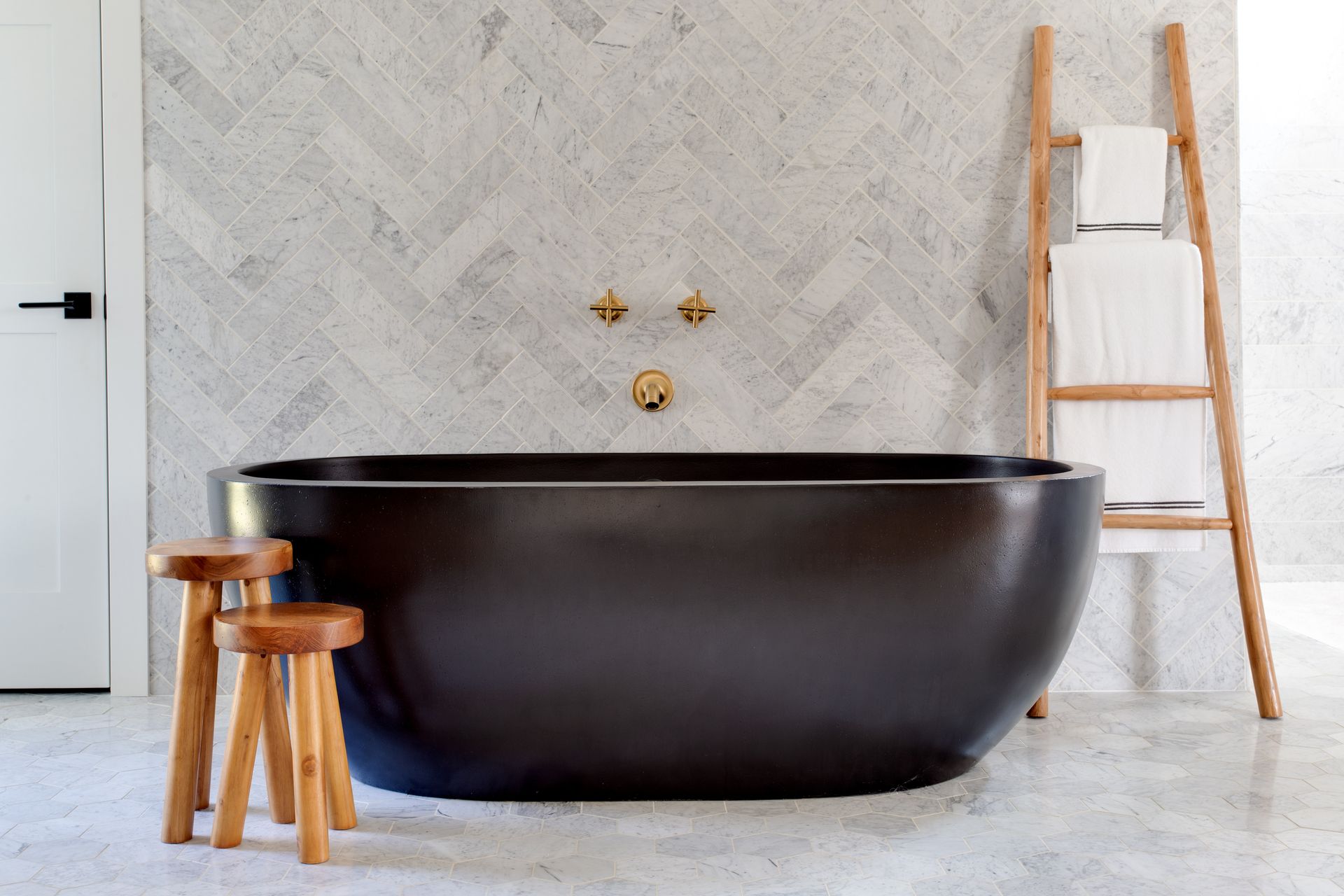 A bathroom with a black bathtub and two wooden stools.
