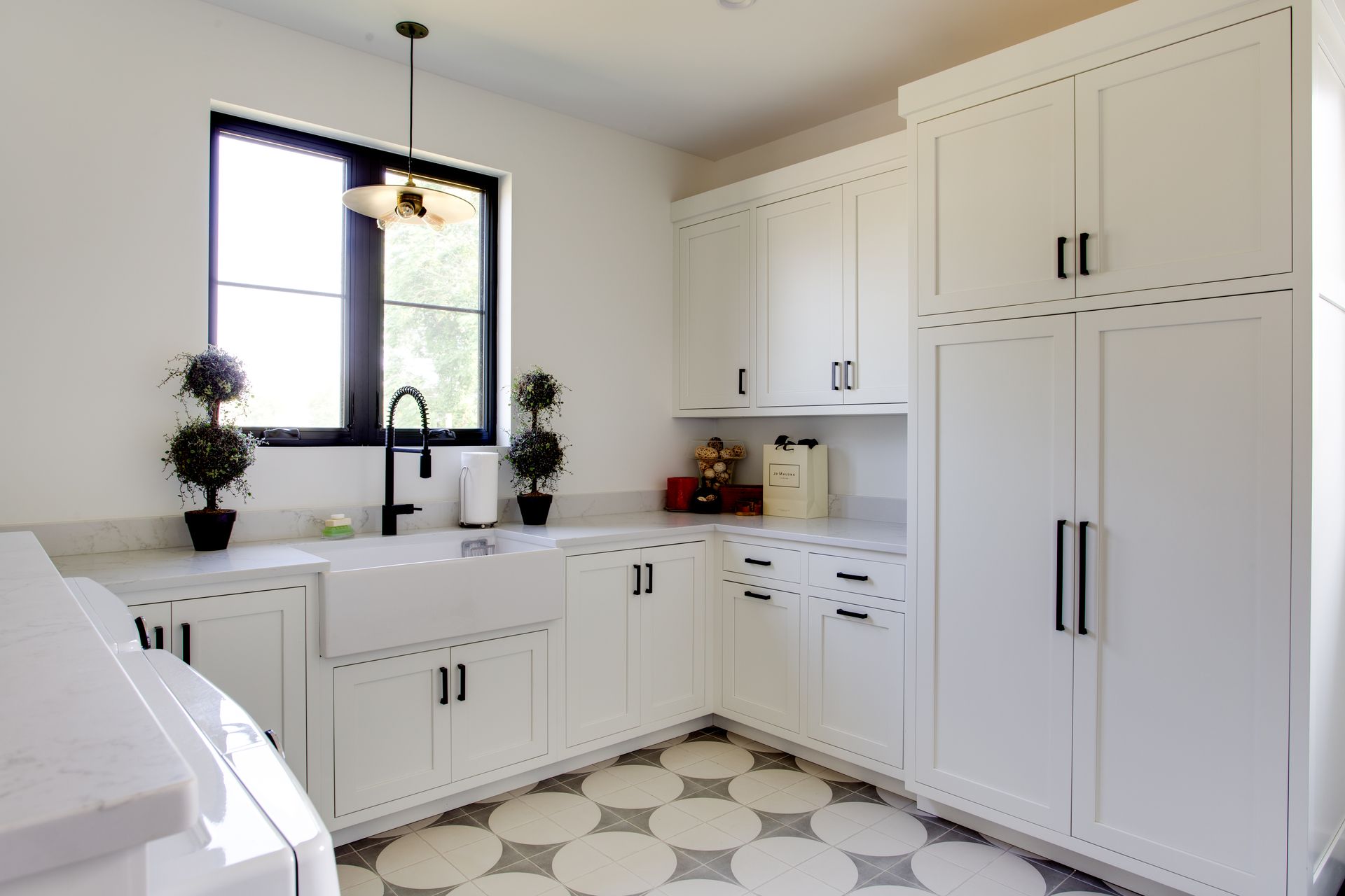 A laundry room with white cabinets and a black window.