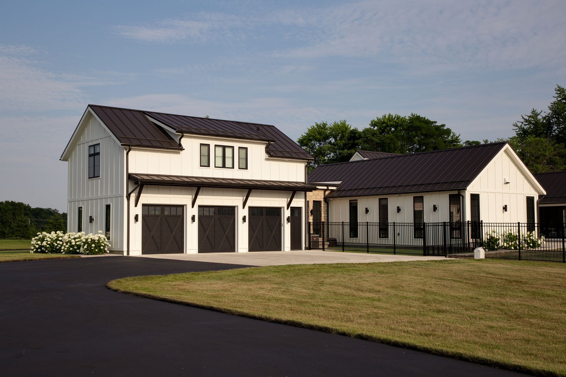 A white house and garage with a black roof is sitting on top of a lush green grass.