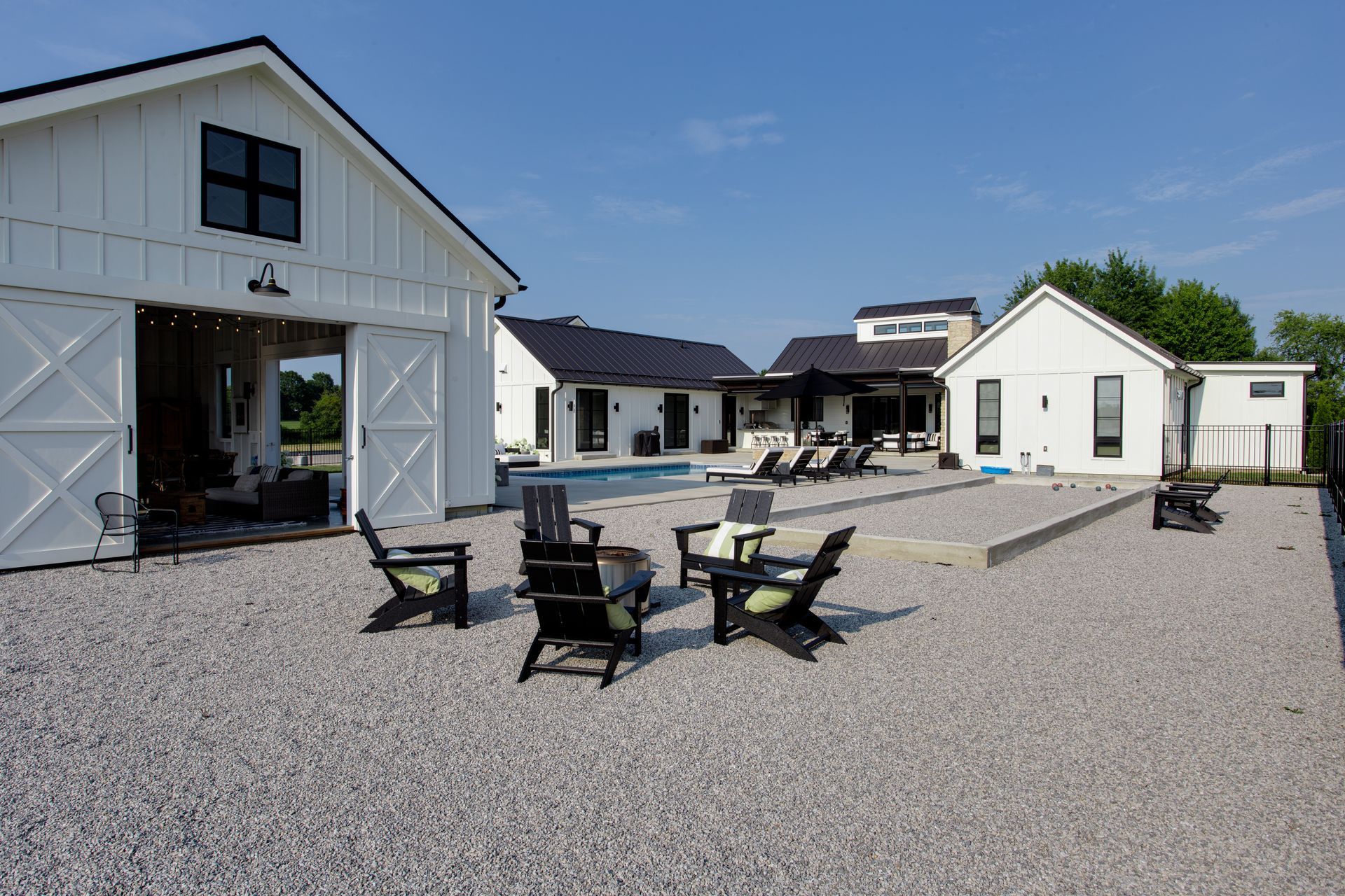 A white barn with a swimming pool and chairs in front of it.