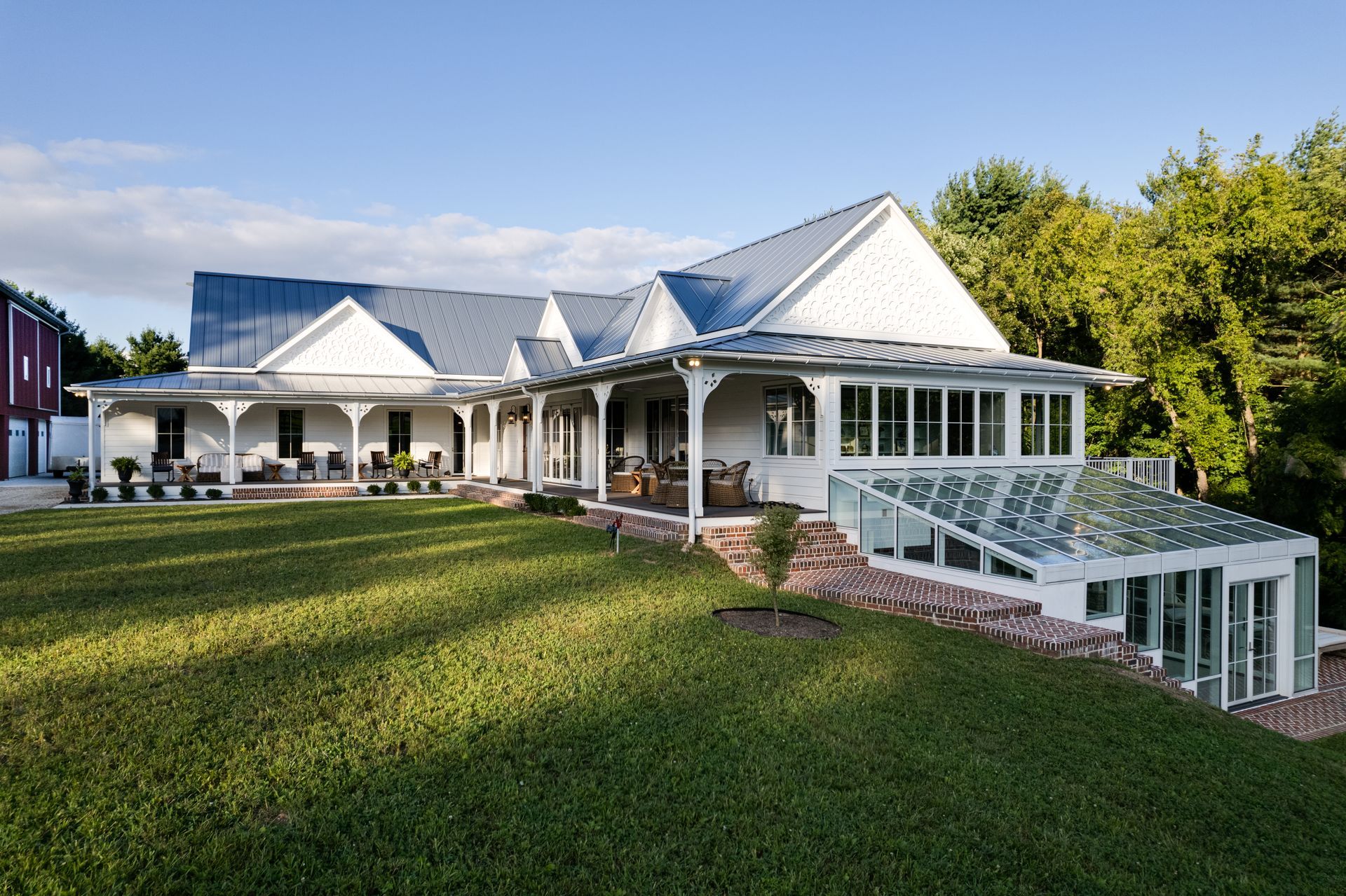 Large white house with wraparound porch and manicured lawn under a blue sky.