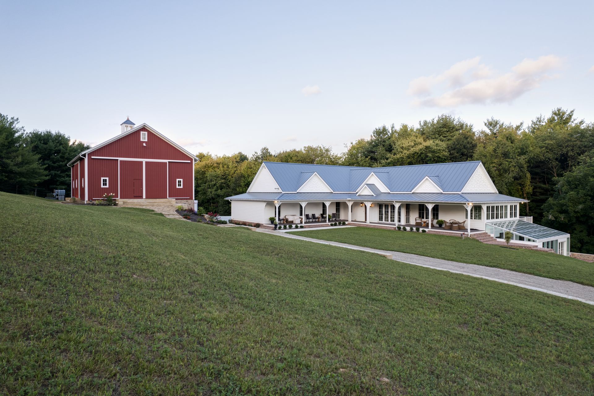 Red barn and white farmhouse on a grassy hillside with trees in the background.