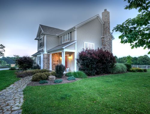 A large house with a stone chimney is sitting on top of a lush green field.