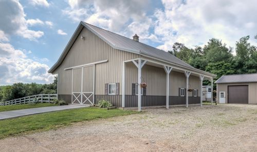 A large barn with a covered porch is sitting on top of a grassy hill.