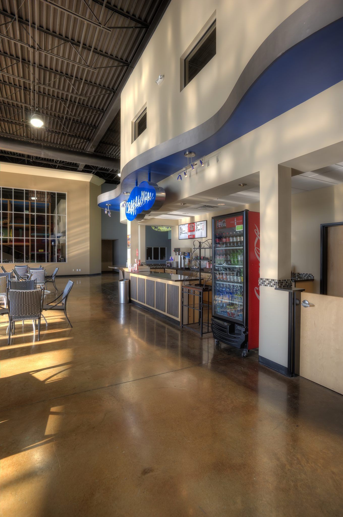 A large room with tables and chairs and a cooler with beverages inside.